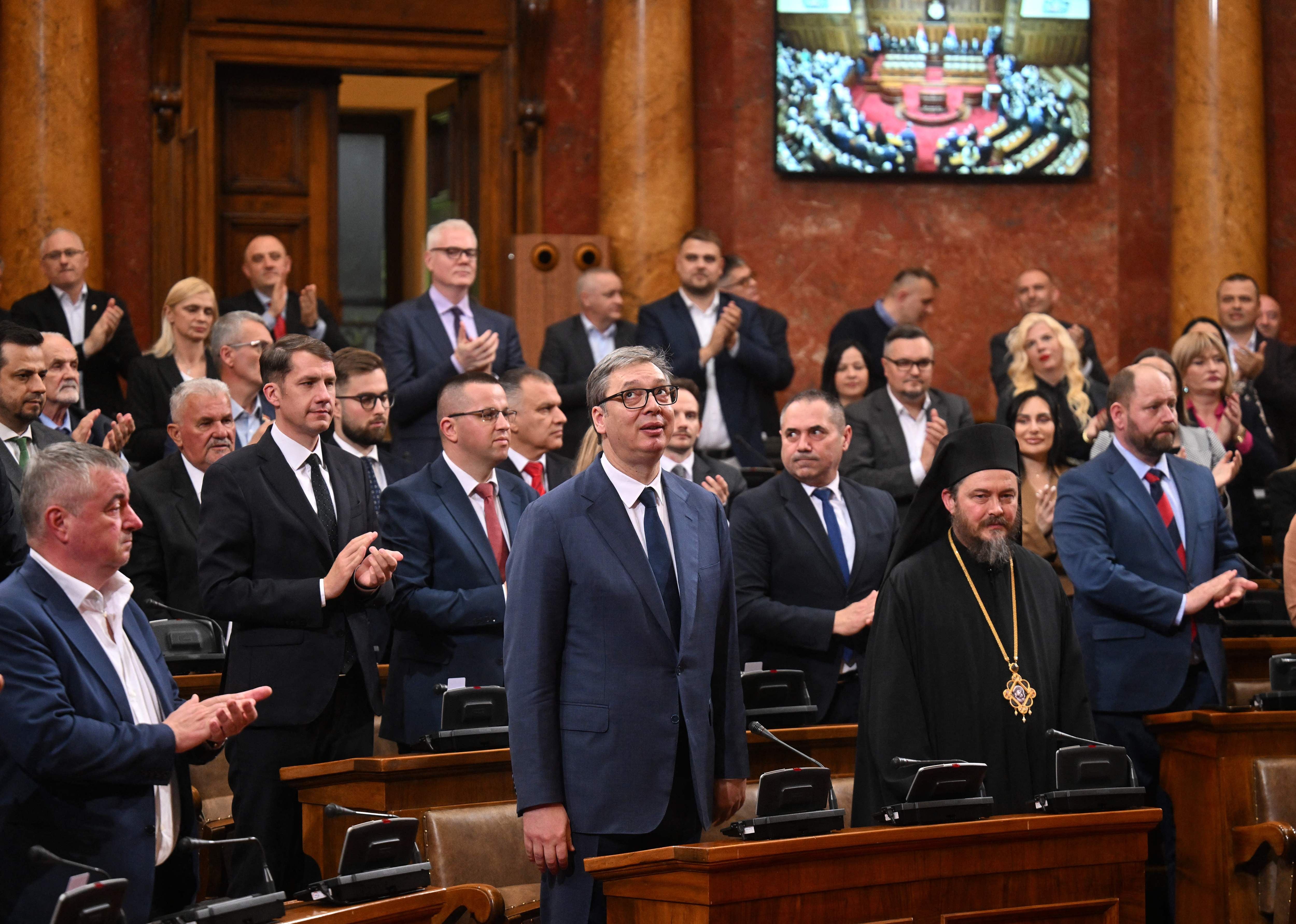 Mehrere Menschen in Anzügen und religiöser Kleidung stehen und applaudieren im Parlament.
