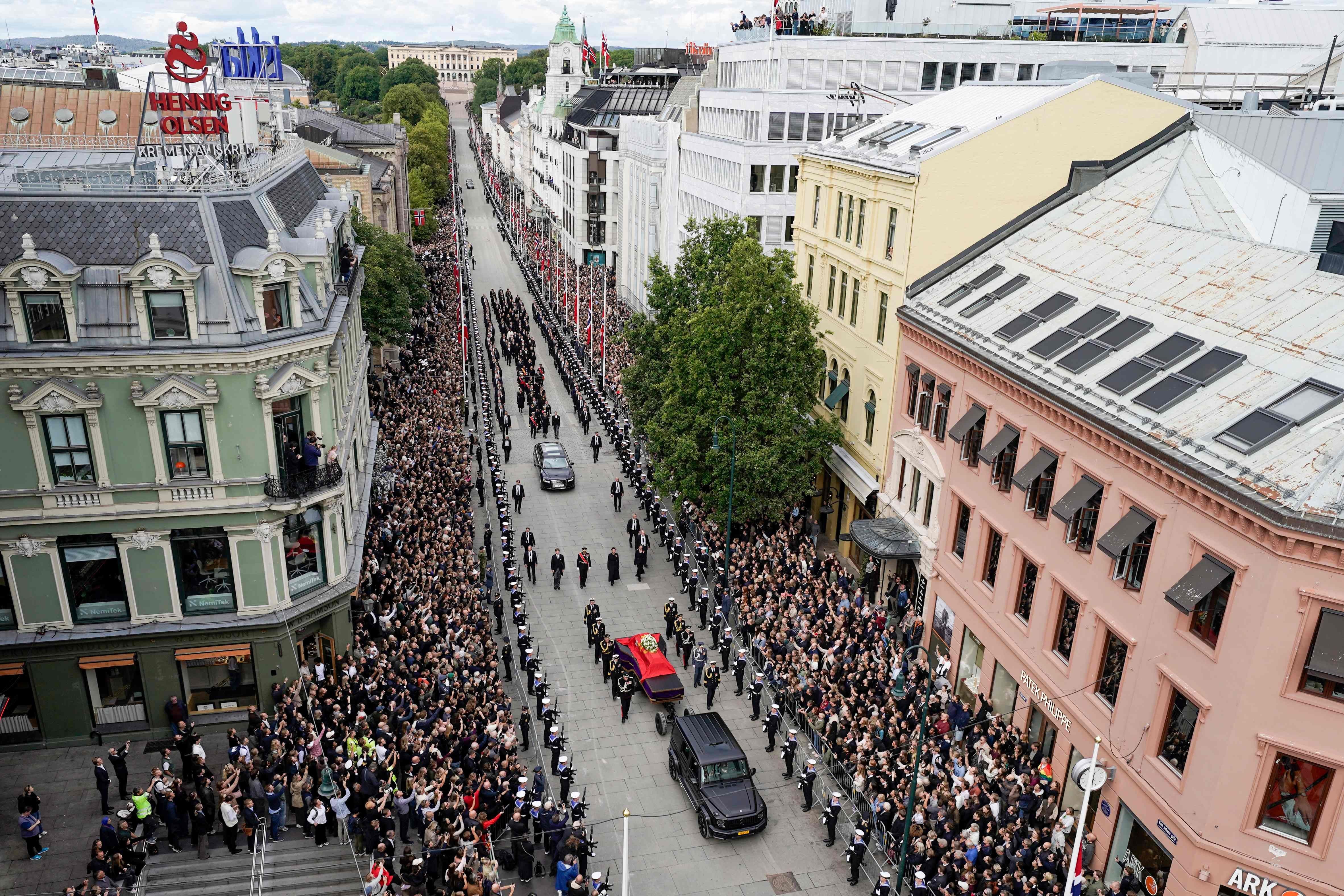 Menschen stehen dicht gedrängt, während ein königlicher Trauerzug mit Sarg durch Oslos Straßen zieht.