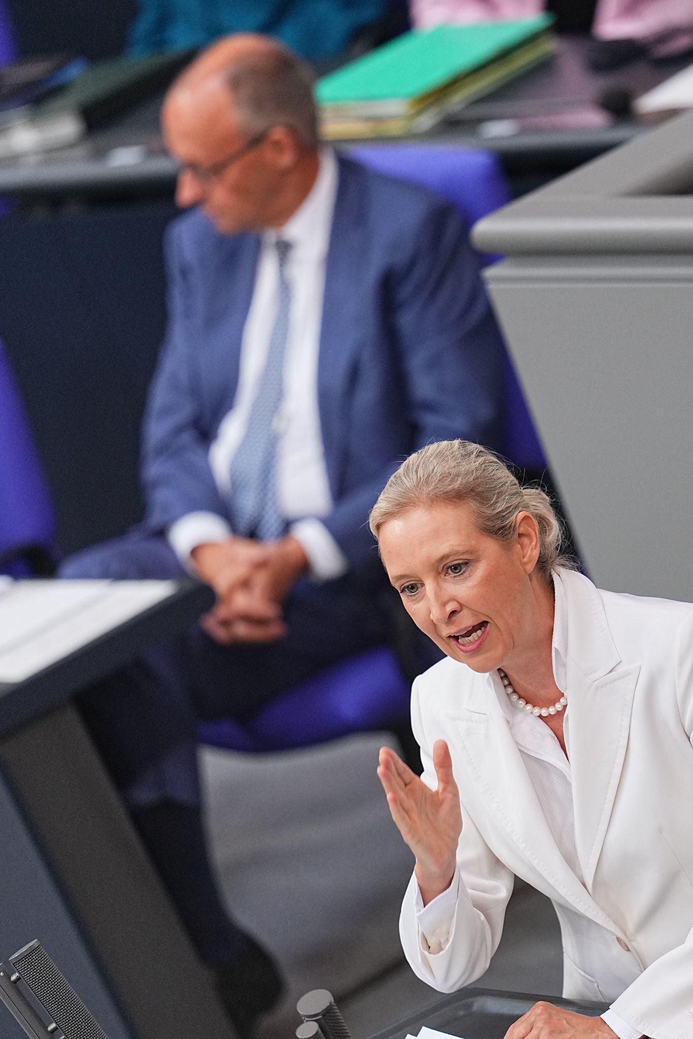 Alice Weidel spricht im Bundestag, im Hintergrund sitzt ein Mann im Anzug.