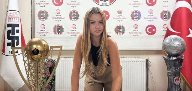 Junge Frau steht zwischen zwei Fußballpokalen und blickt in die Kamera.