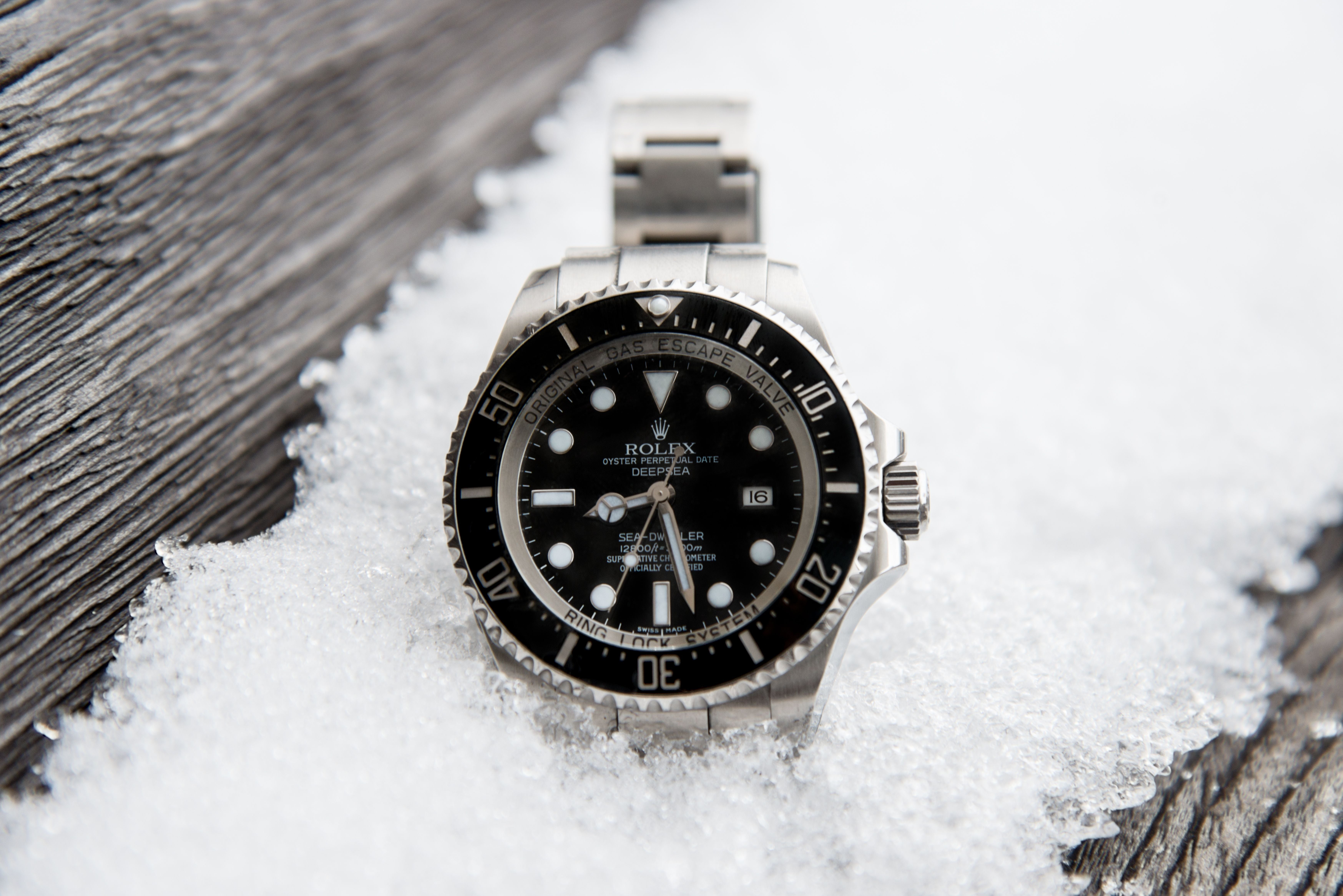 Rolex DEEPSEA Uhr liegt auf schneebedecktem, altem Holzbrett im Freien.