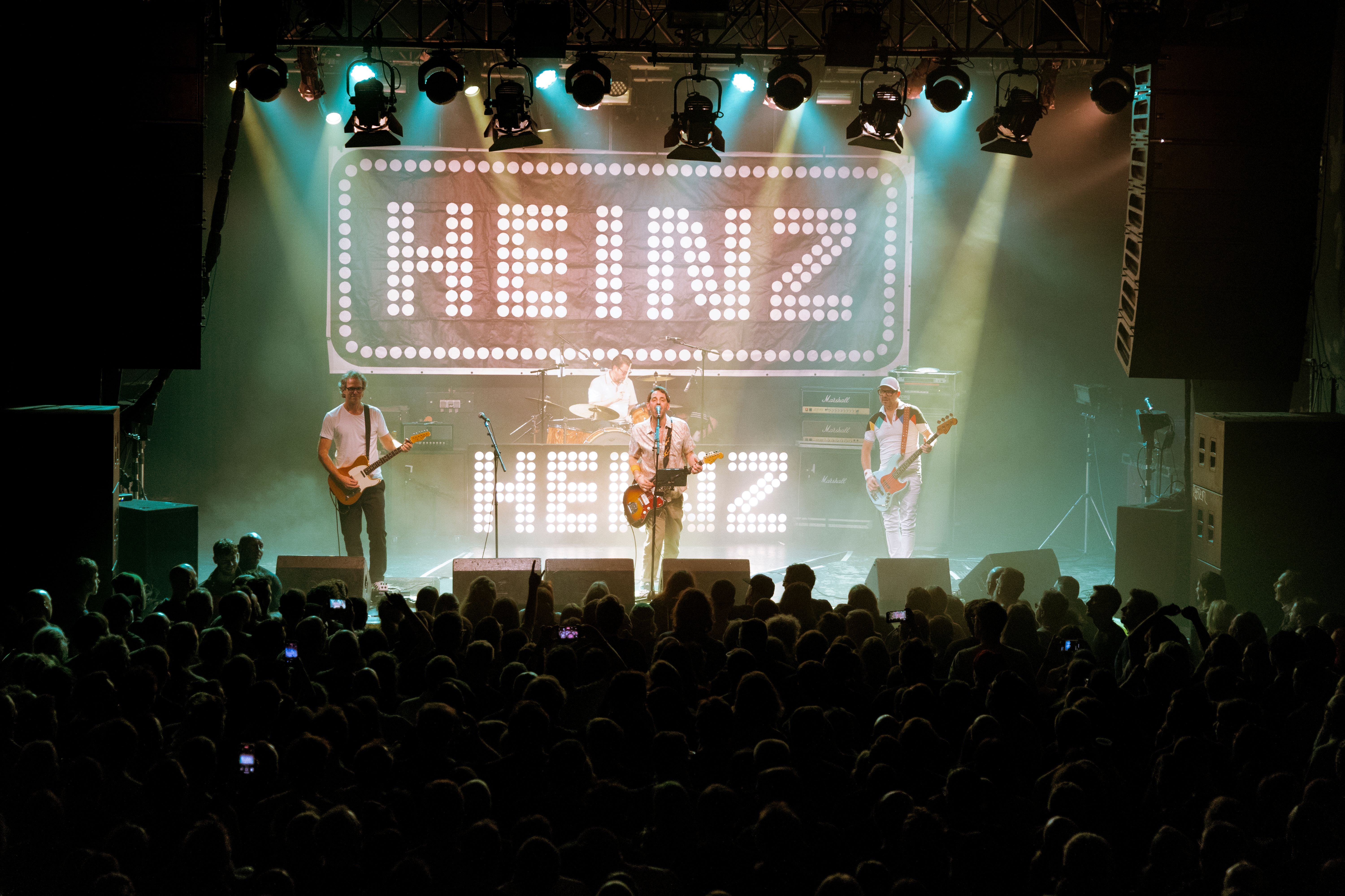 Konzert von Heinz aus Wien mit großem Leuchtschild "HEINZ" und Publikum im Vordergrund.