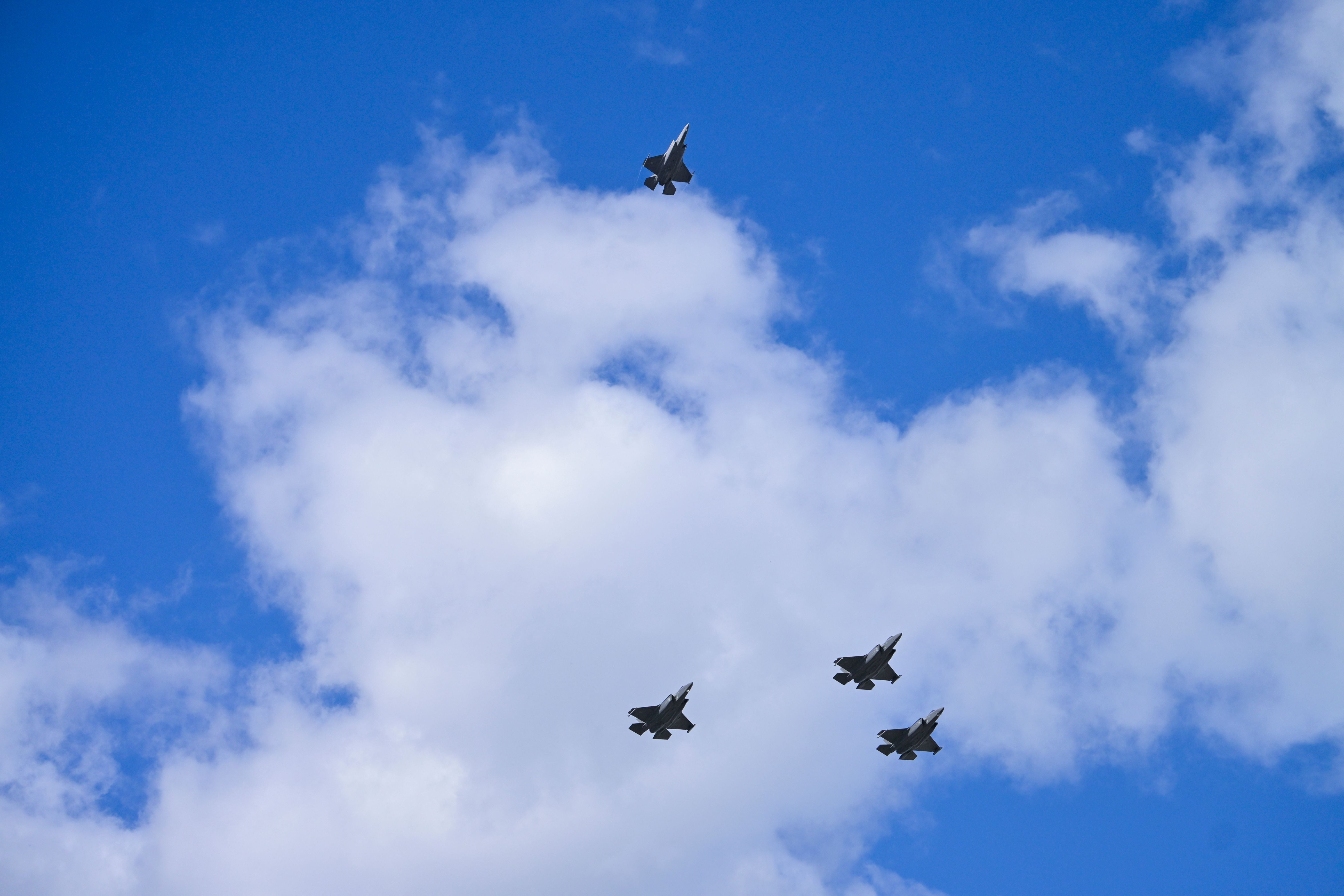 Vier Kampfjets fliegen in einer Formation am Himmel mit weißen Wolken.