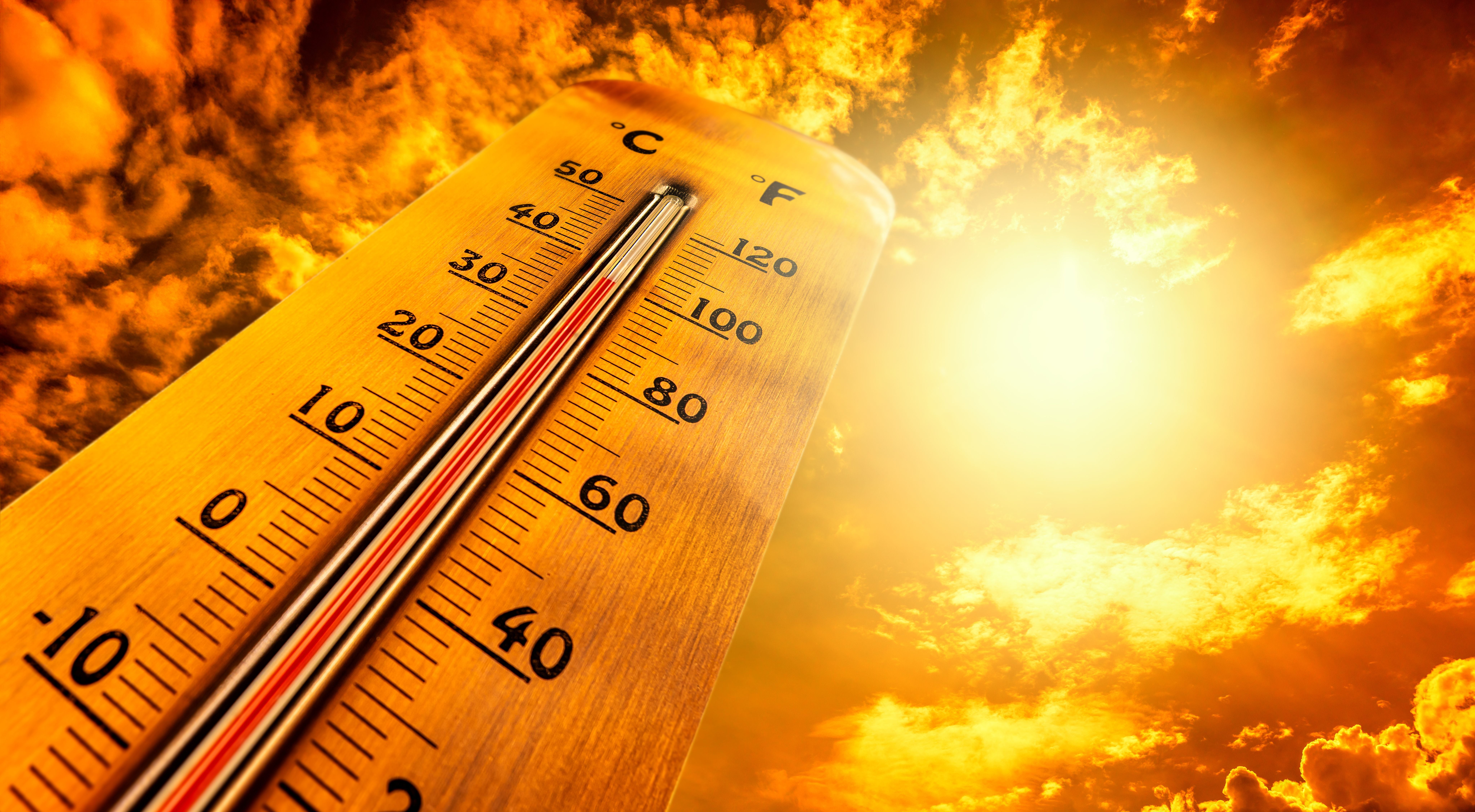 Ein Thermometer zeigt hohe Temperaturen vor einem sonnigen, orangefarbenen Himmel.