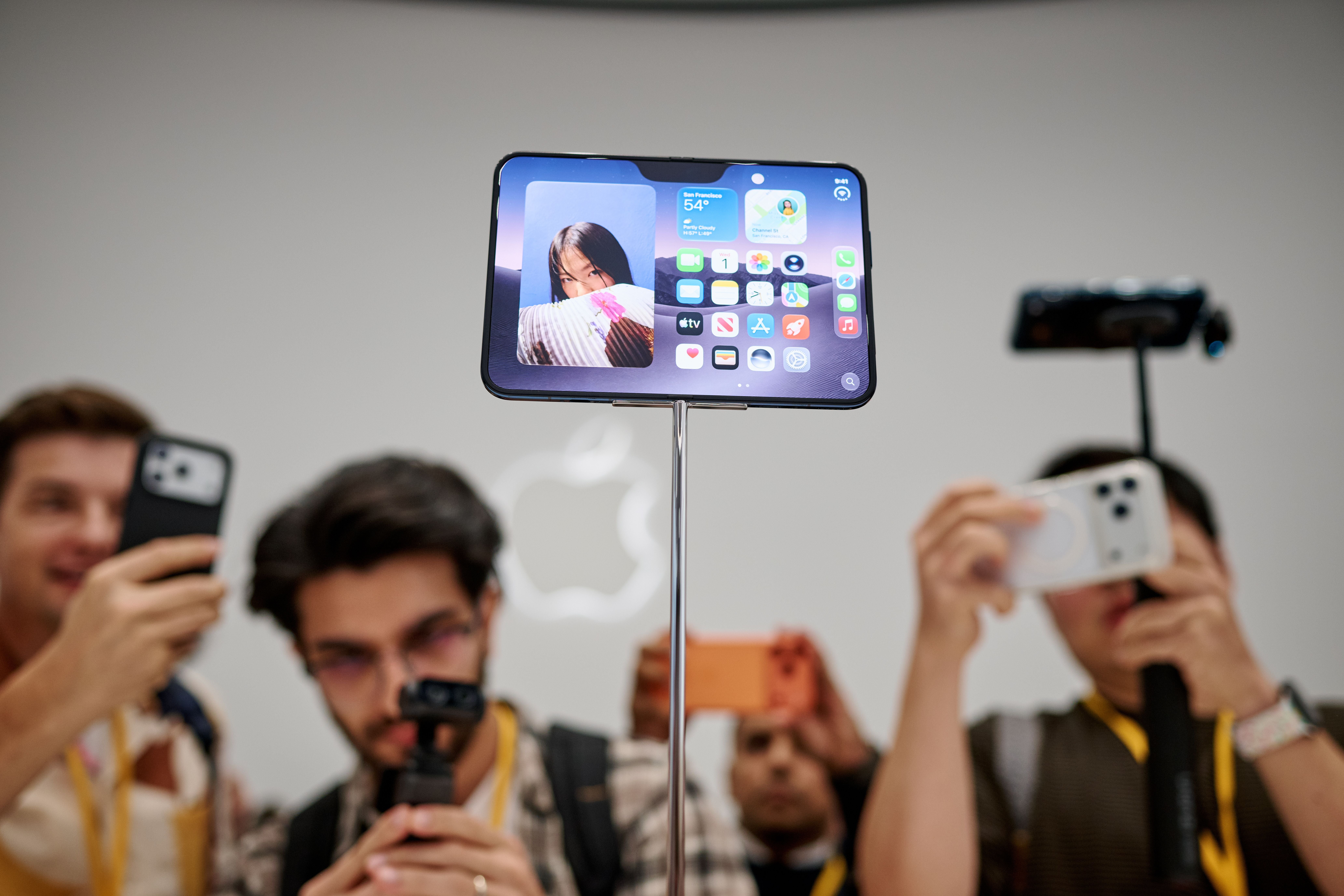 Menschen fotografieren ein ausgestelltes, aufgeklapptes faltbares iPhone bei einer Apple-Veranstaltung.