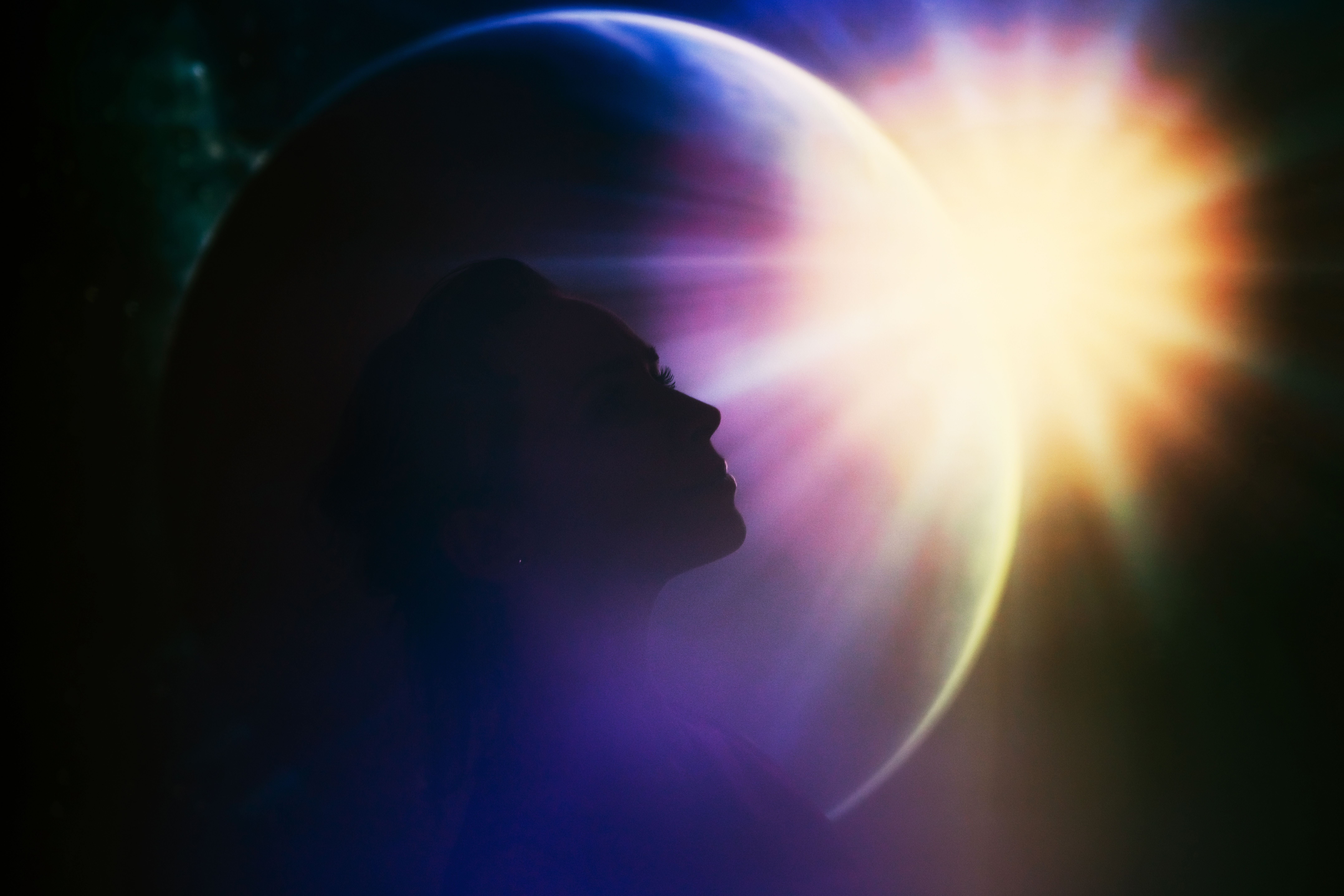 Die Silhouette einer Frau vor einem leuchtenden Planeten und strahlender Sonne im Hintergrund.
