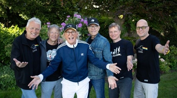 Sechs fröhliche Männer posieren gemeinsam im Garten und lächeln in die Kamera.