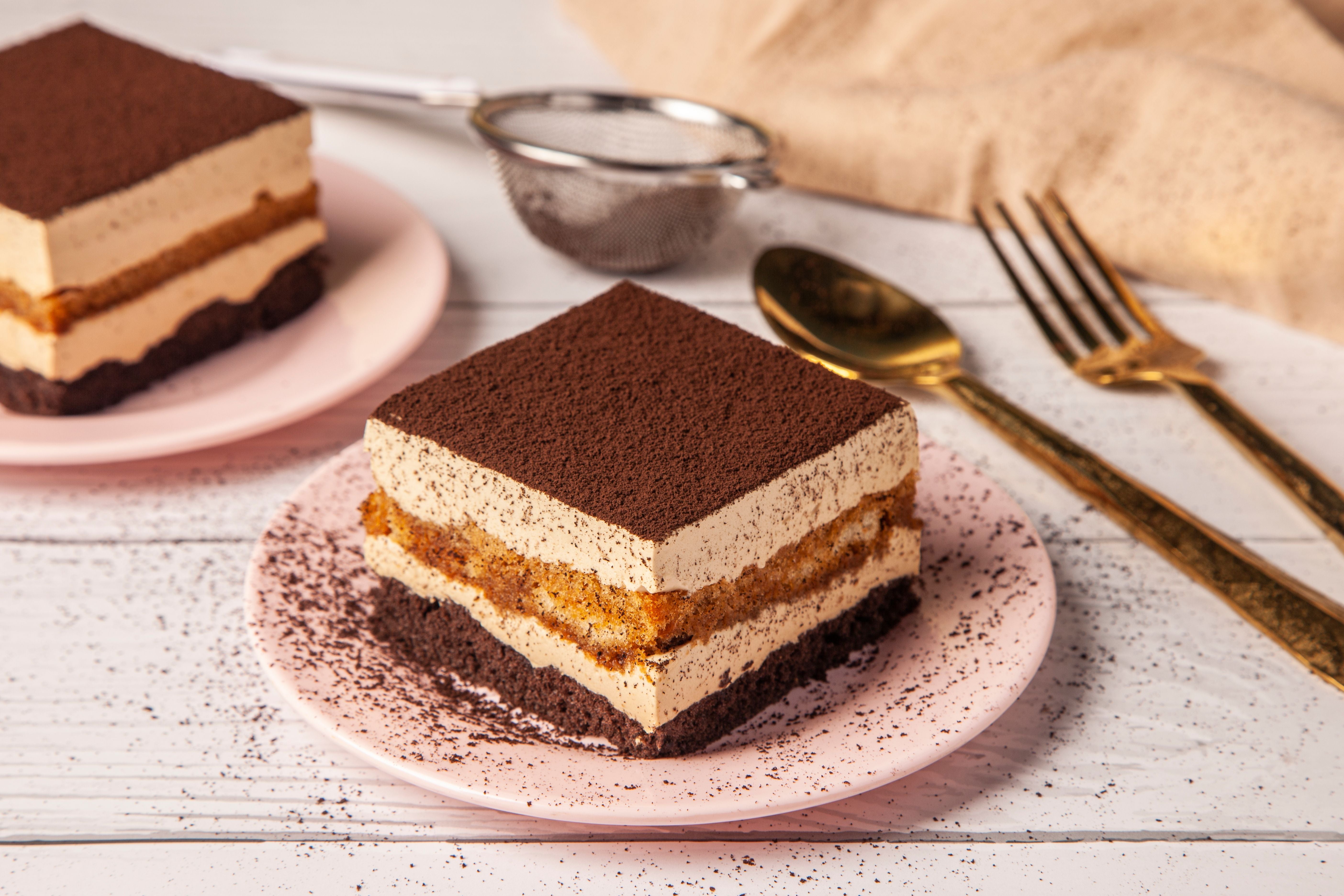 Ein Stück Tiramisu-Brownie auf einem rosafarbenen Teller, daneben goldenes Besteck.