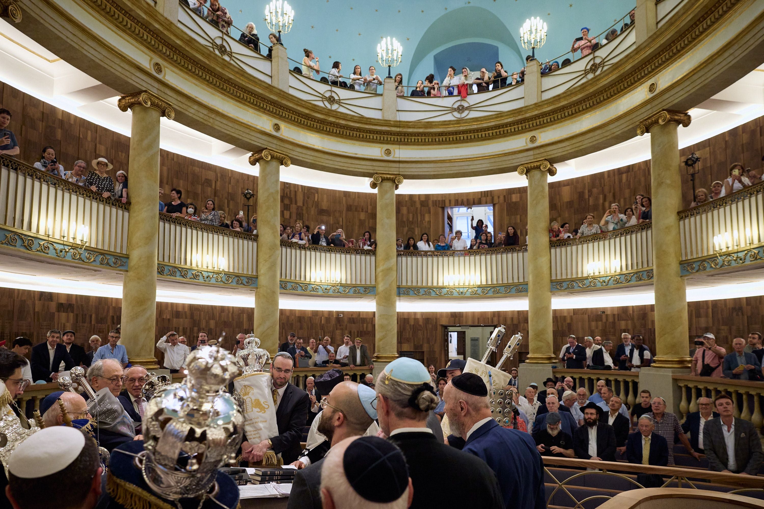 Viele Menschen feiern die Wiedereröffnung einer Synagoge in einem großen, prunkvollen Saal.