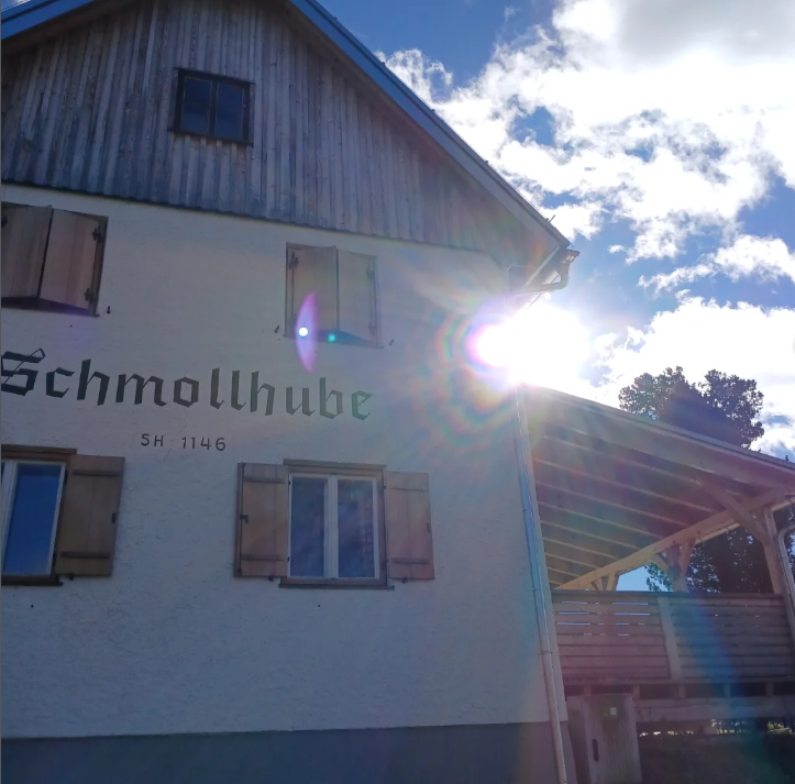 Haus mit Schriftzug „Schmollhube“ und Sonnenschein am Giebel unter blauem Himmel.