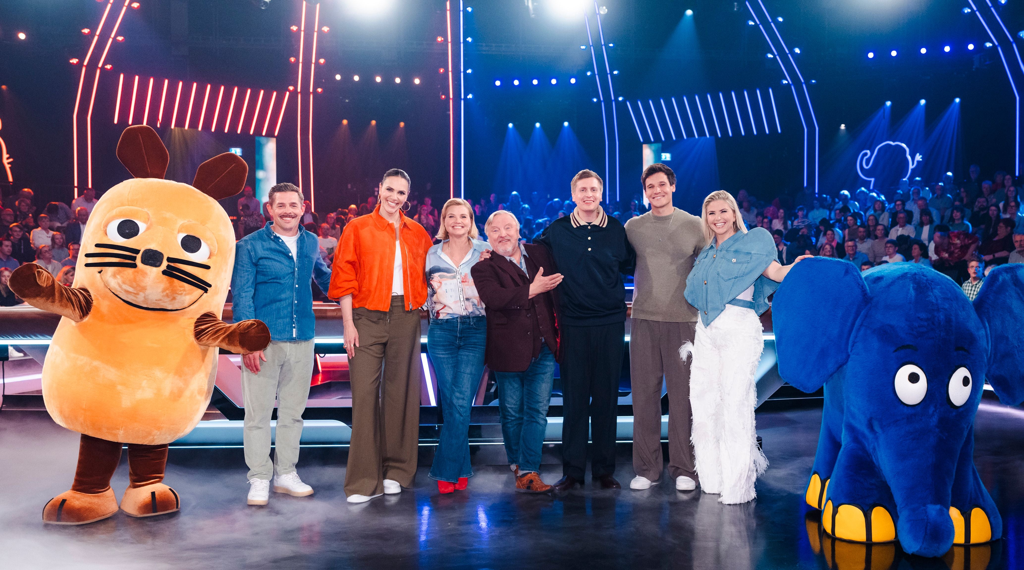 Mehrere Menschen posieren mit den Maus- und Elefant-Kostümen vor Publikum in einer TV-Show.