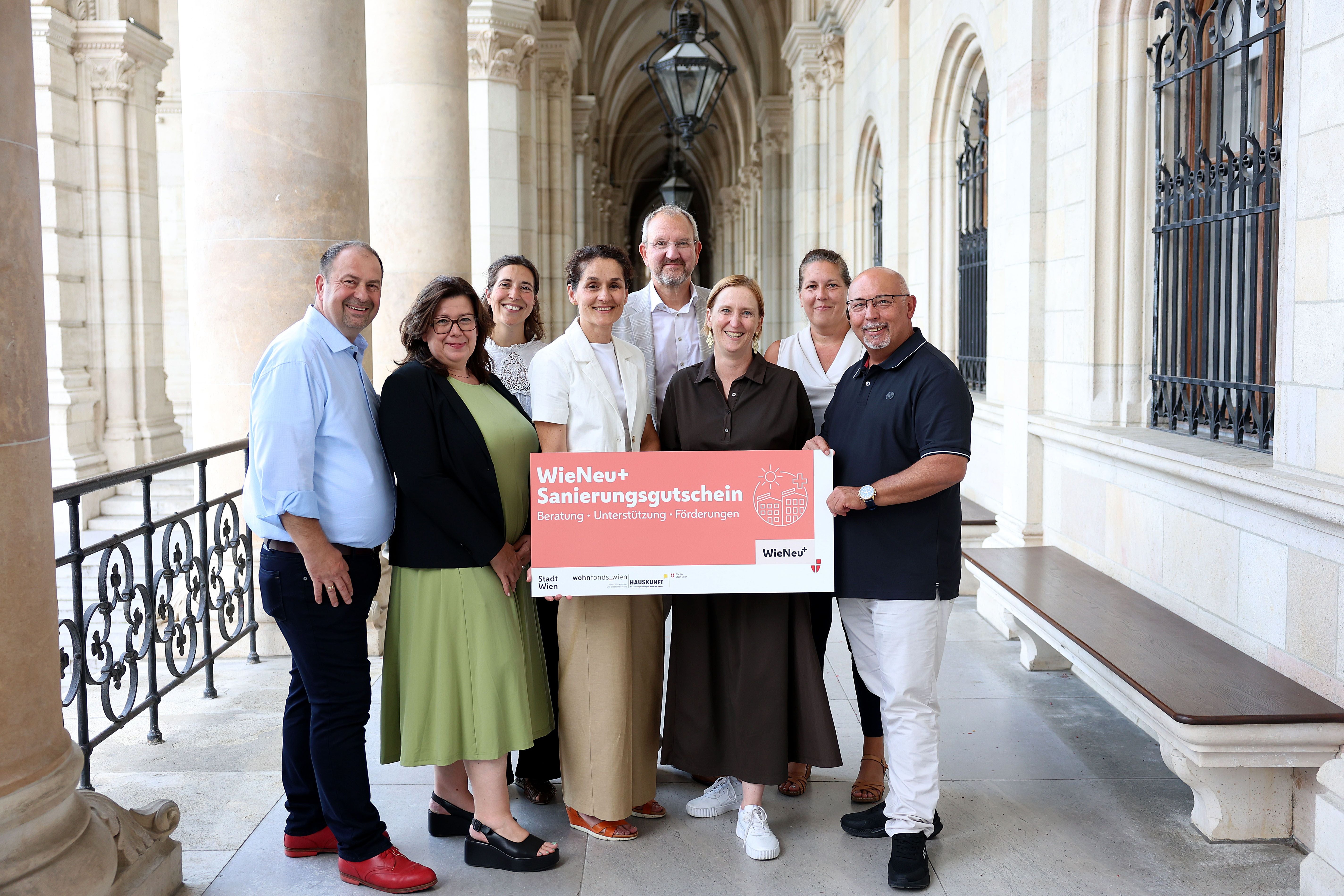 Eine Gruppe von Menschen hält ein Schild mit der Aufschrift „Sanierungsgutschein“.