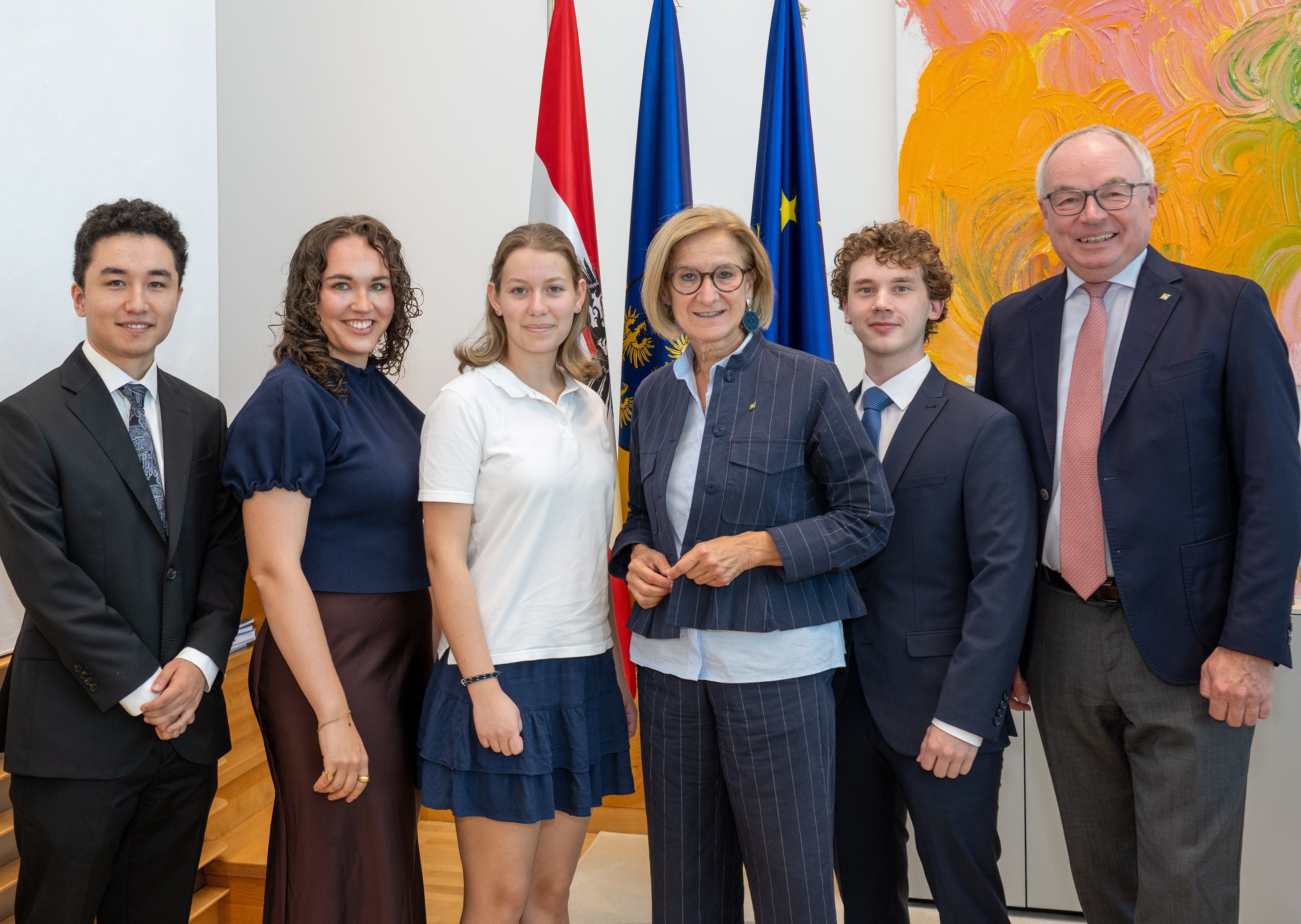 Sechs Personen stehen lächelnd vor österreichischen und EU-Flaggen.
