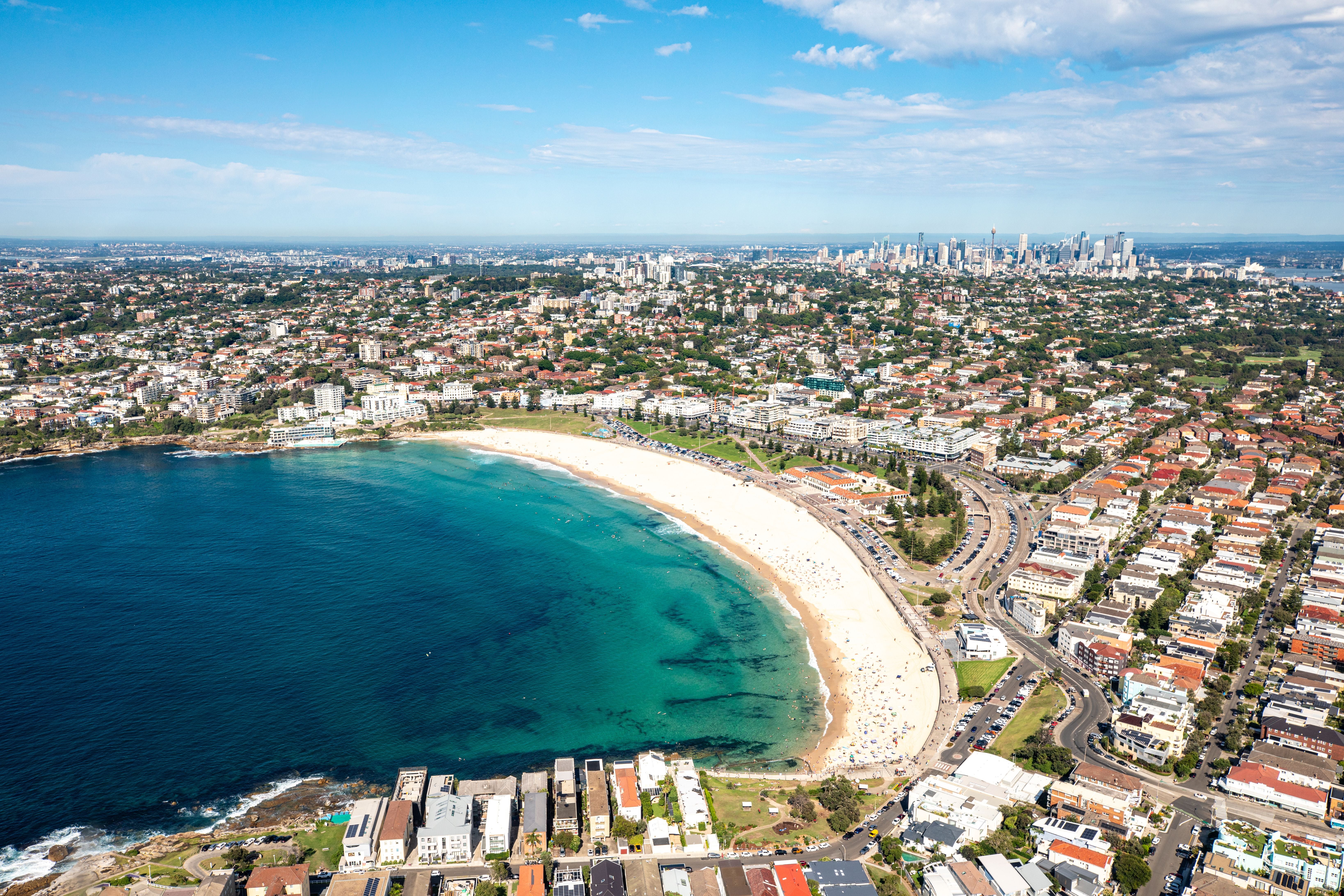 Luftaufnahme vom Bondi Beach in Sydney mit Stadt und Geschäftsviertel im Hintergrund.