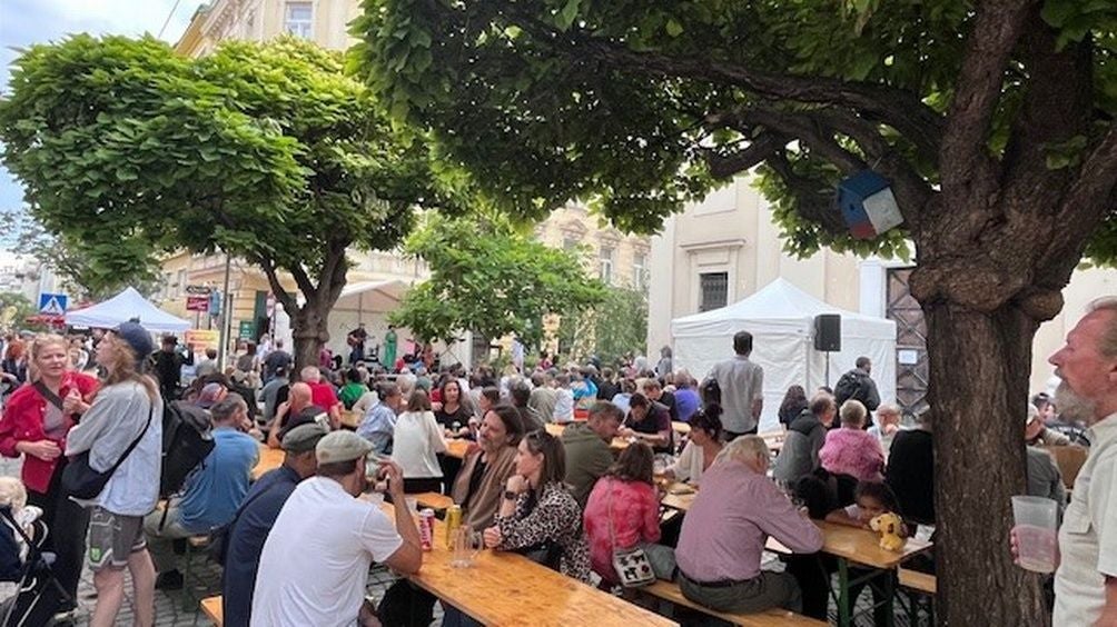 Viele Menschen sitzen und stehen an Biertischen unter Bäumen beim Reindorfgassenfest.