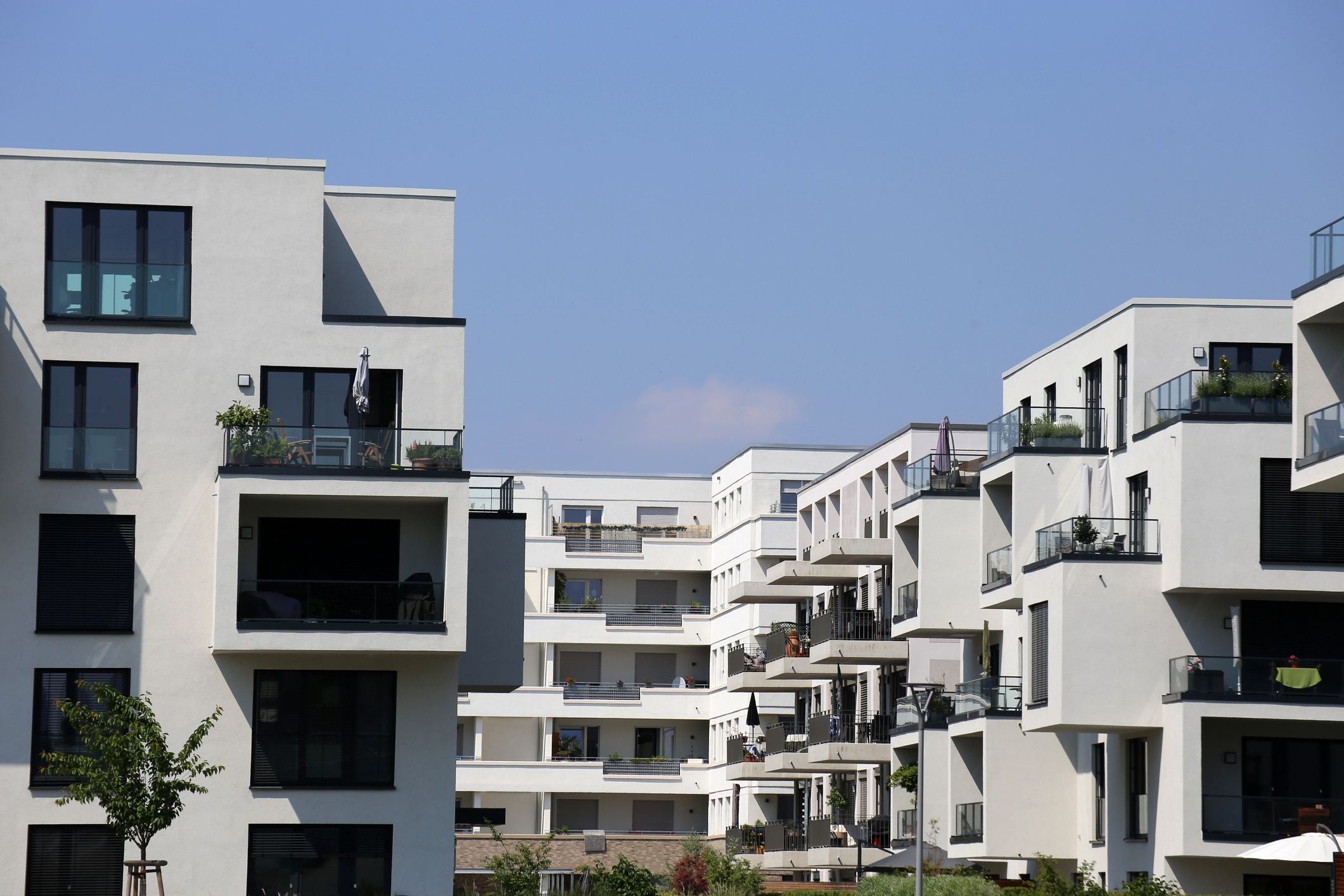 Moderne Wohnanlage mit mehreren weißen Mehrfamilienhäusern und Balkonen bei blauem Himmel.