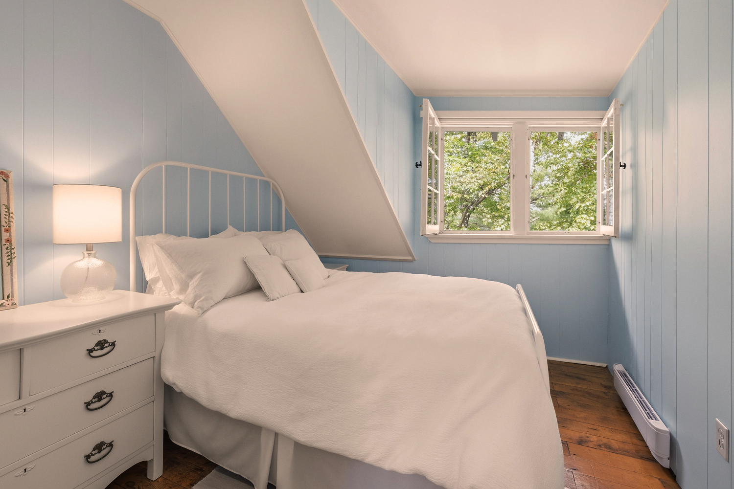 Kleines Schlafzimmer mit blau gestrichenen Wänden, Doppelbett und offenem Fenster mit Blick ins Grüne.