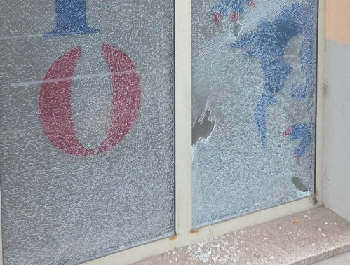 Zerbrochene Fensterscheibe mit Rissen und herausgeschlagenem Loch, Glassplitter am Boden.