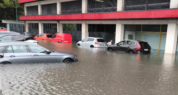 Mehrere Autos stehen in einer tief überfluteten Straße vor einem Gebäude.
