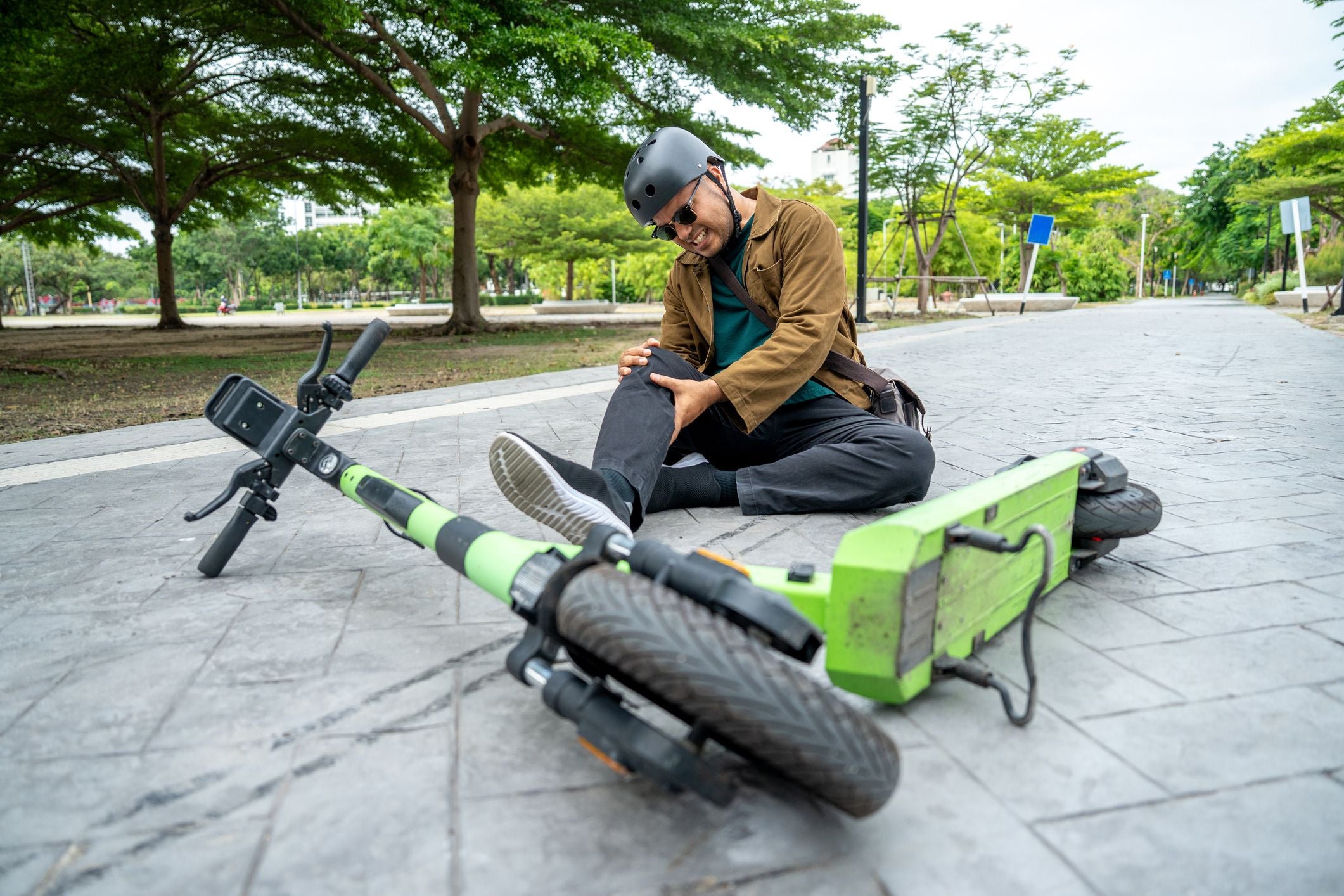 Mann sitzt nach Sturz mit Elektro-Scooter auf der Straße und hält schmerzhaft sein Bein.