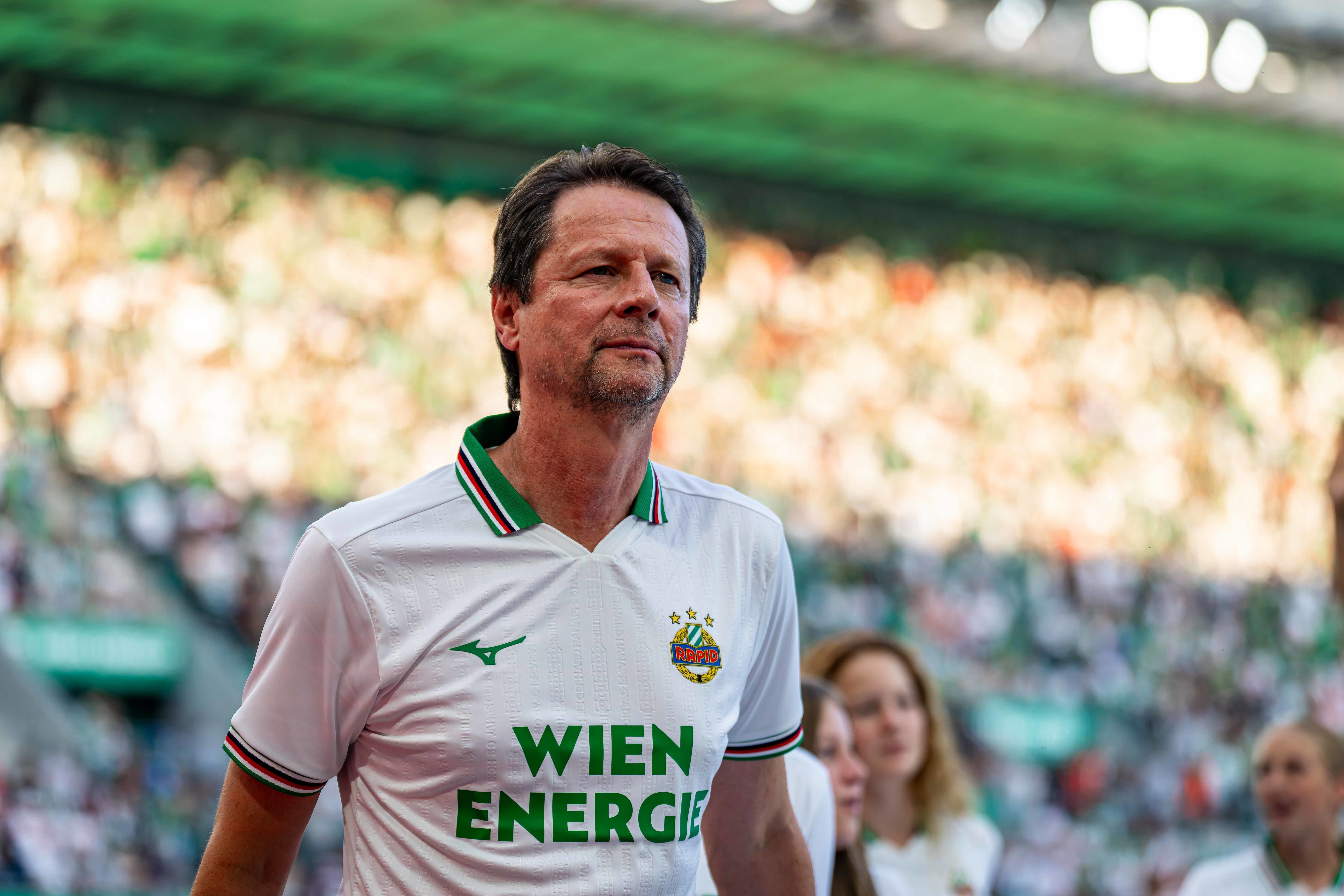 Peter Schöttel im weißen Retro-Trikot von Rapid Wien schaut nachdenklich ins Stadionpublikum.