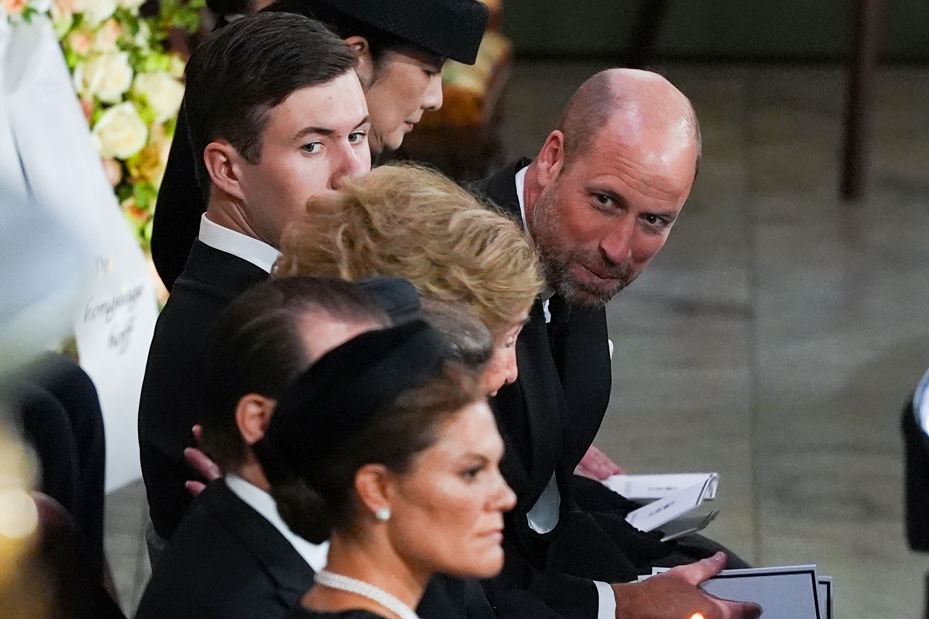 Mehrere elegant gekleidete Menschen sitzen nebeneinander bei einer Trauerfeier in einer Kirche.