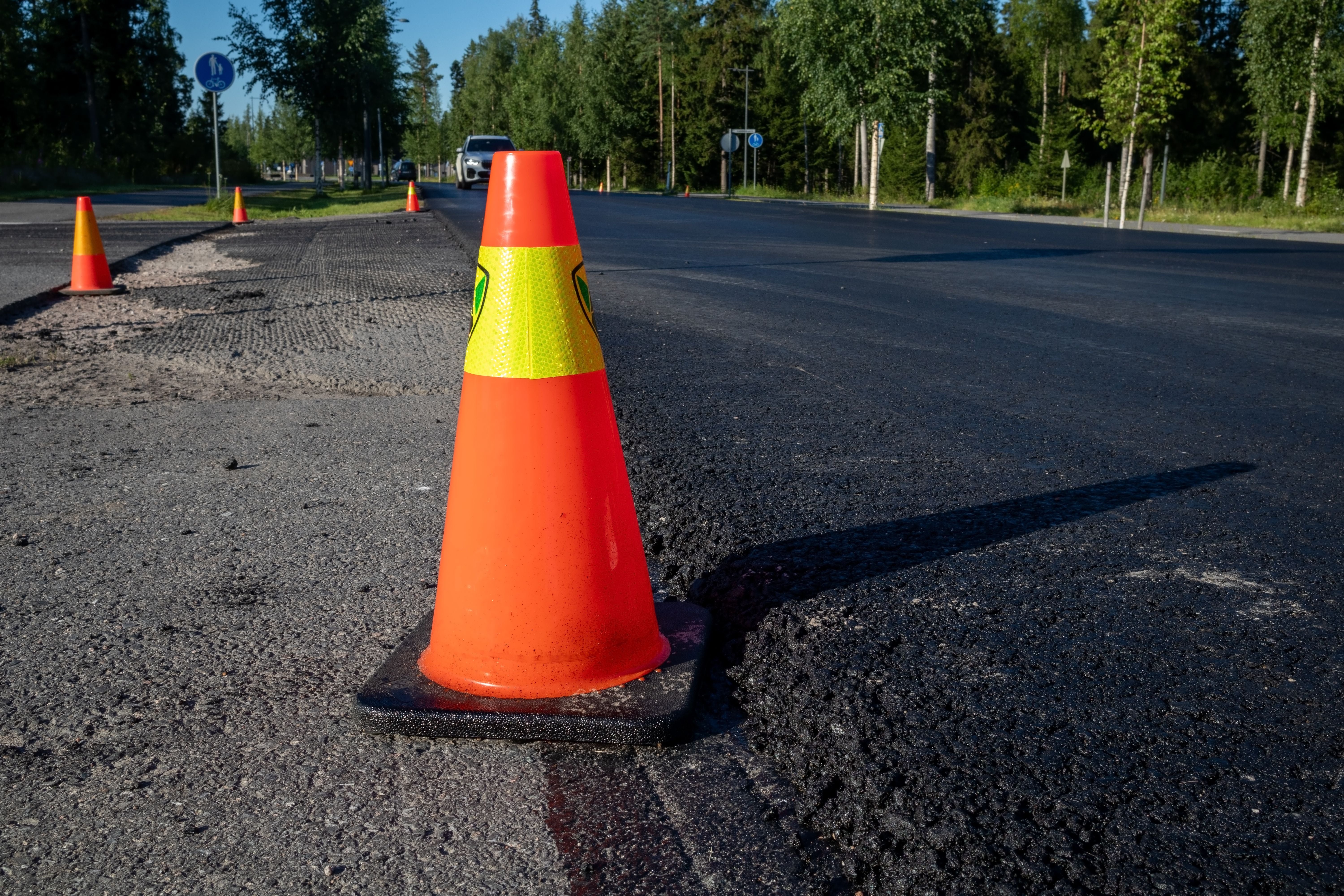 Leuchtend orangefarner Verkehrskegel steht bei frischem Asphalt auf einer Straße.