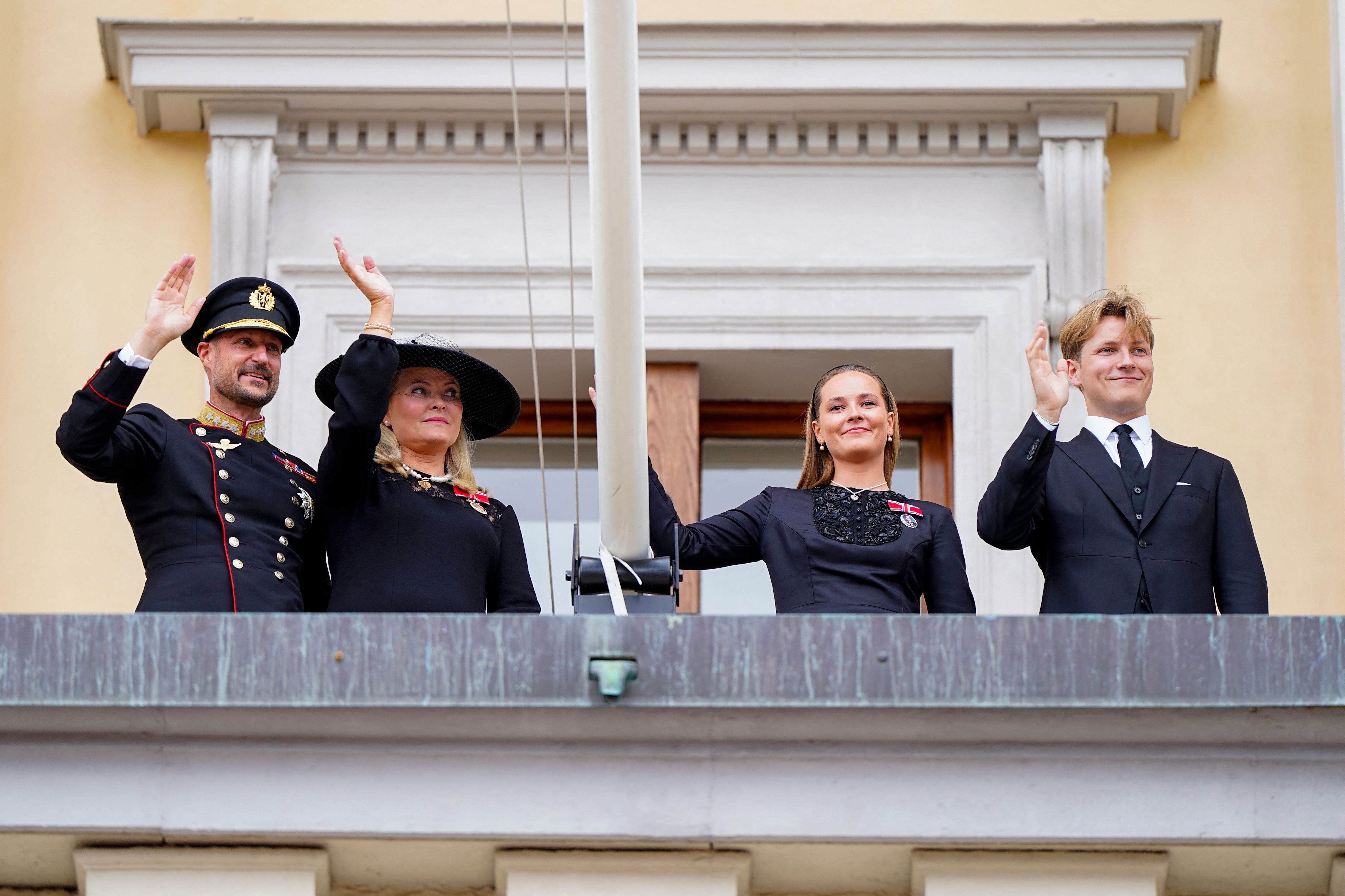 Vier Personen der norwegischen Königsfamilie winken in schwarzer Kleidung von einem Balkon.