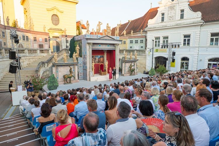 Zuschauer sitzen vor einer Freilichtbühne bei den Festspielen Stockerau im Innenhof.