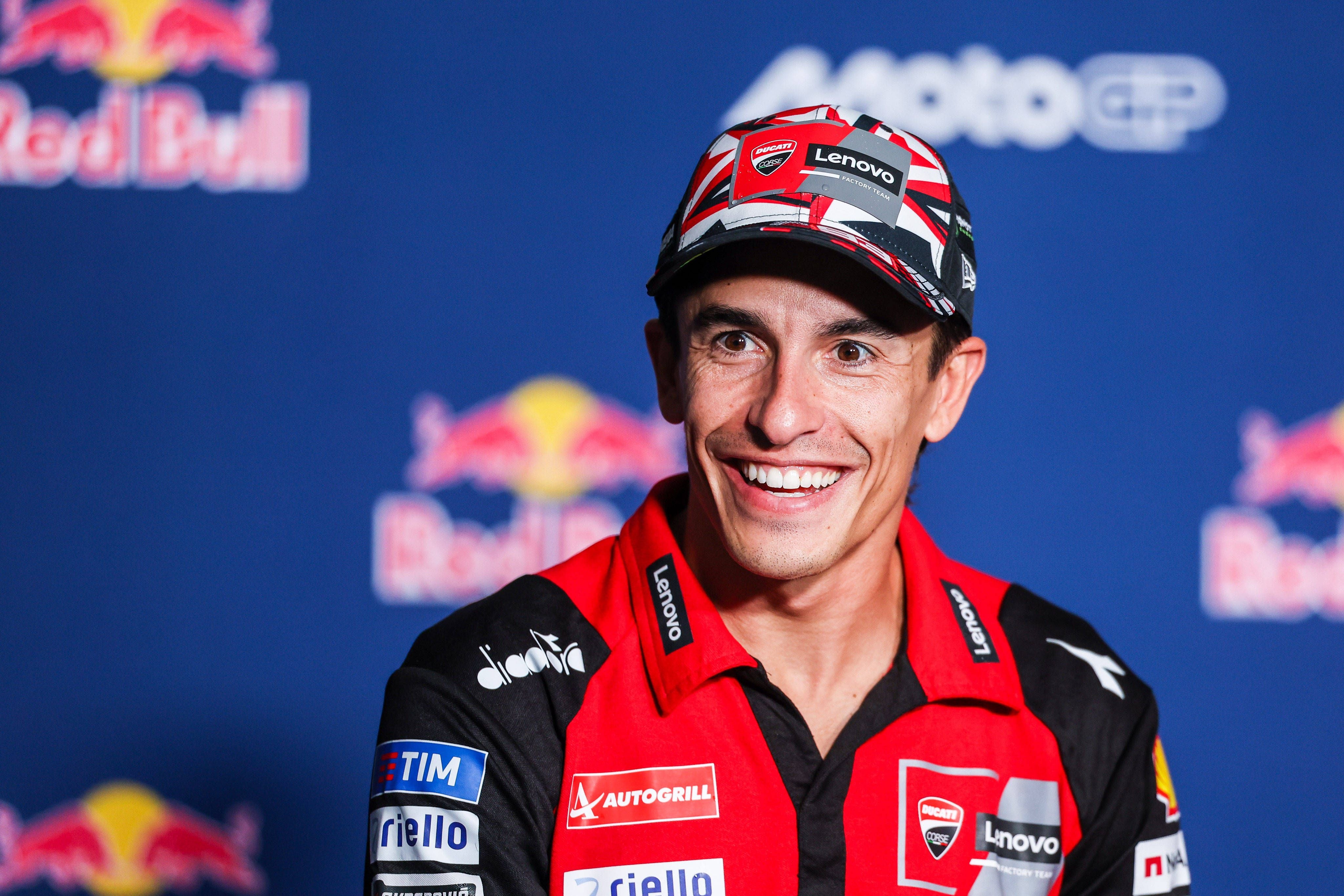 MotoGP-Star Marc Marquez lächelt im rot-schwarzen Ducati-Teamoutfit mit Cappy vor einer Red-Bull-Sponsorenwand.