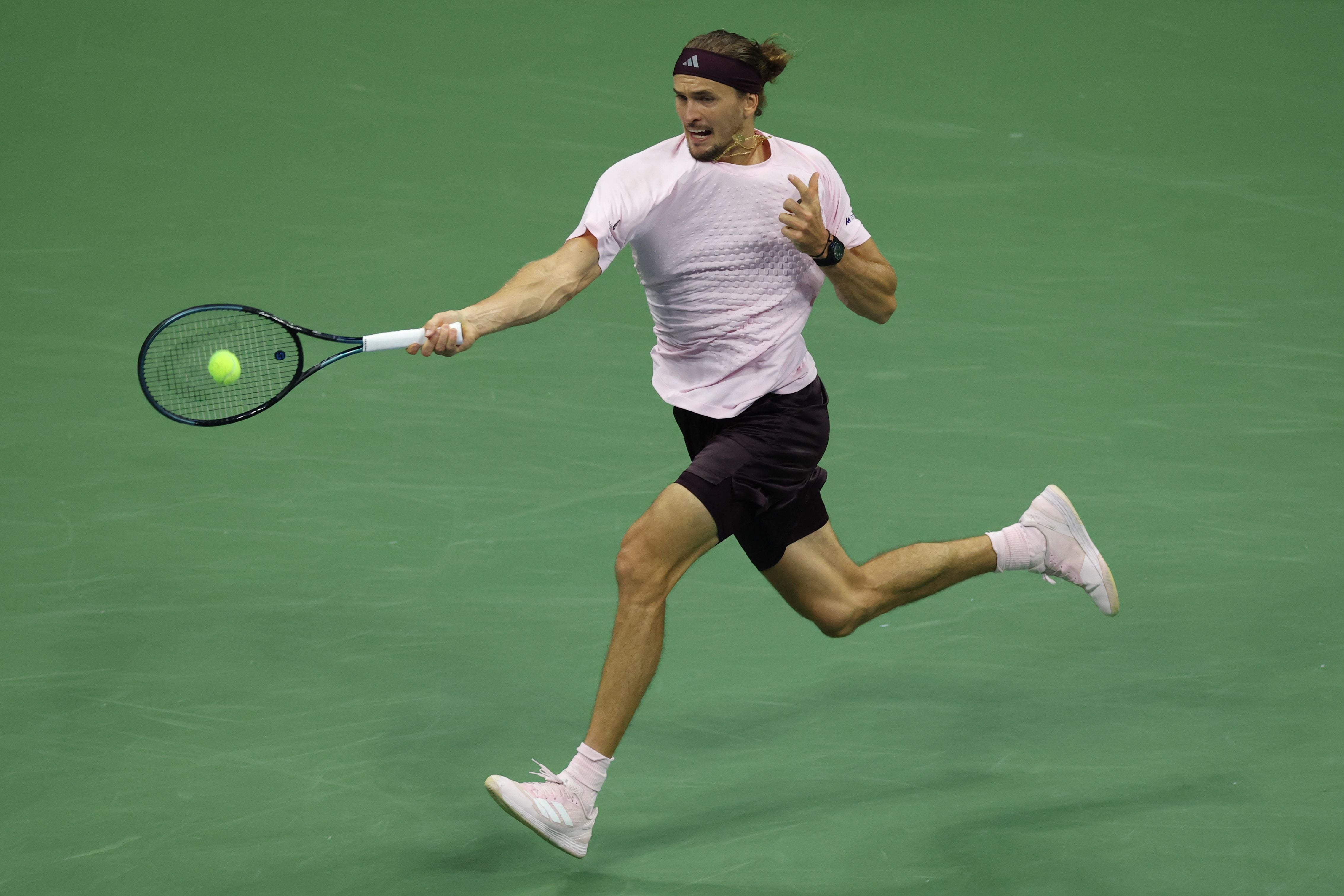 Ein Tennisspieler schlägt auf grünem Hartplatz einen Ball mit einem Vorhandschlag.