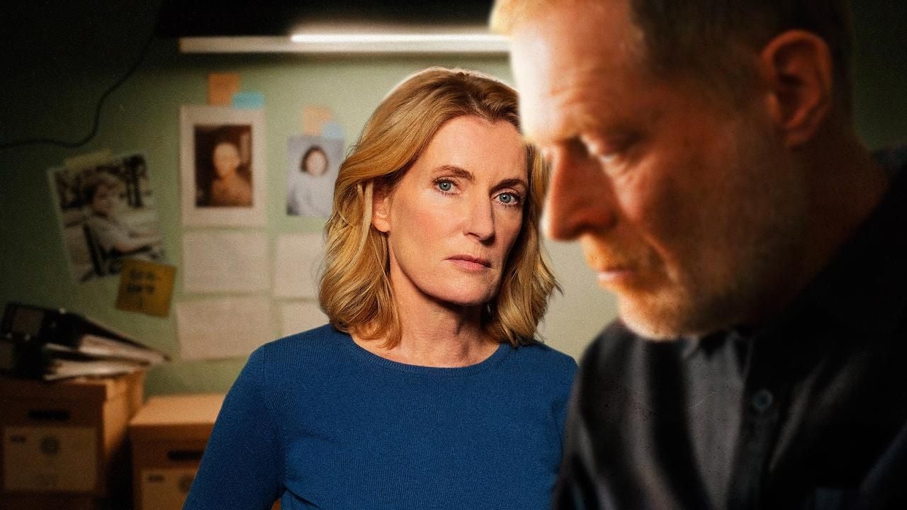 Eine Frau in blauem Pullover blickt ernst, ein Mann ist unscharf im Vordergrund zu sehen.