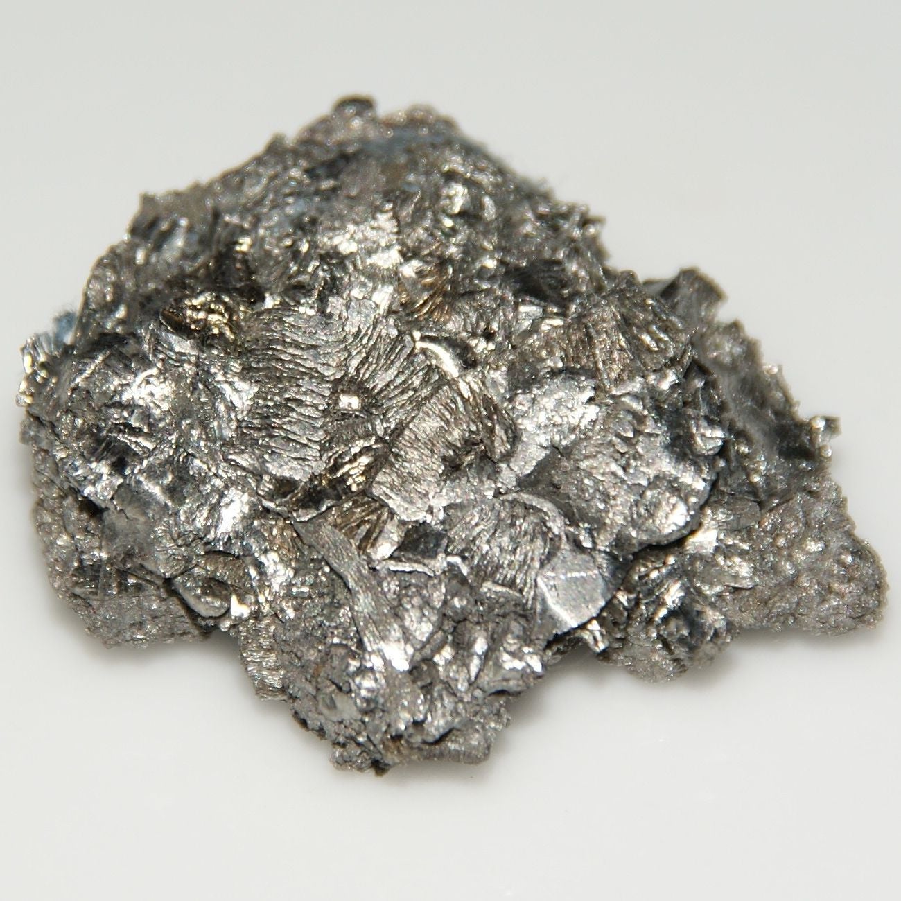 Silberglänzendes, kristallines Metallstück auf weißem Hintergrund.