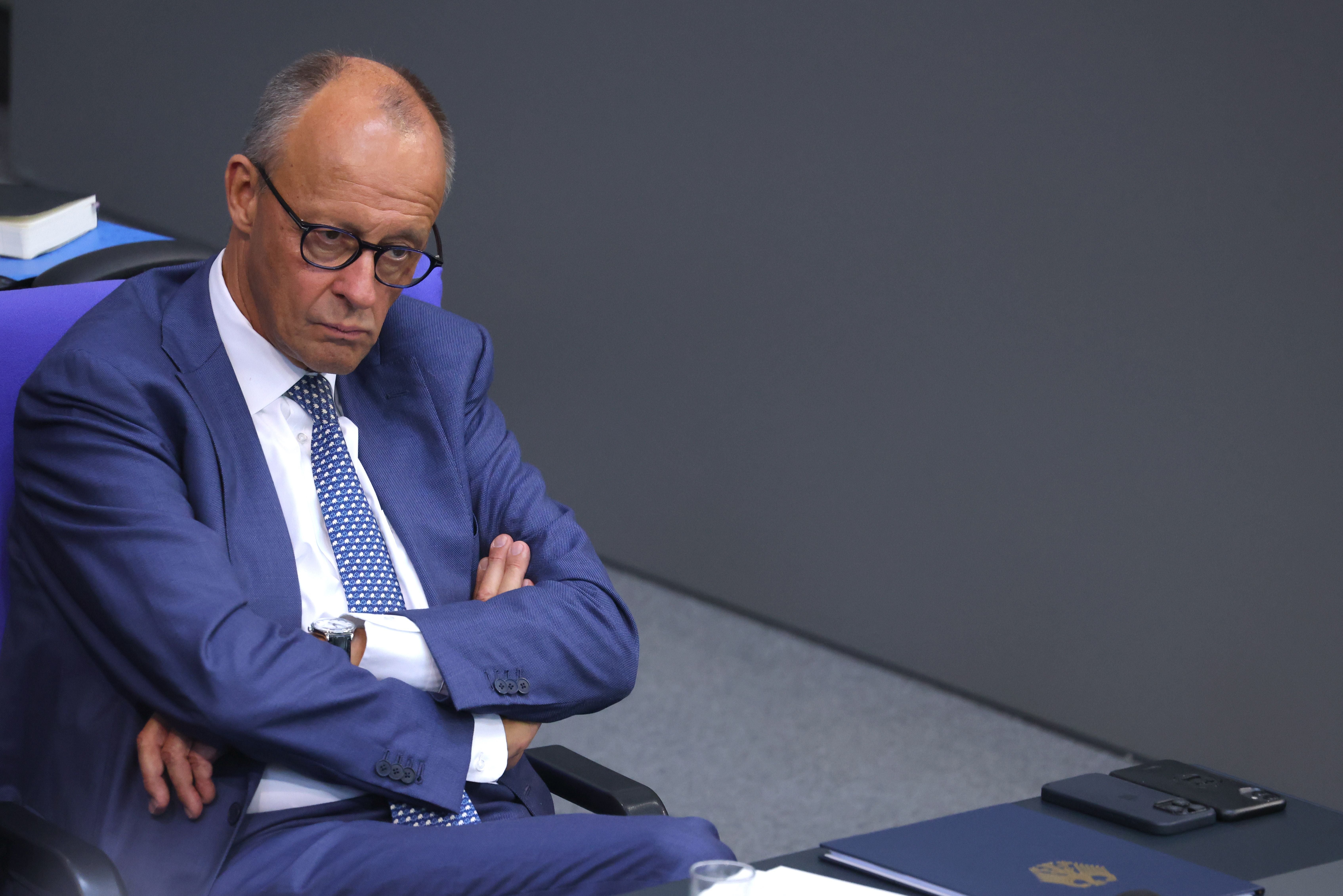 Ein Mann im blauen Anzug sitzt mit verschränkten Armen und ernstem Blick auf einem Stuhl.