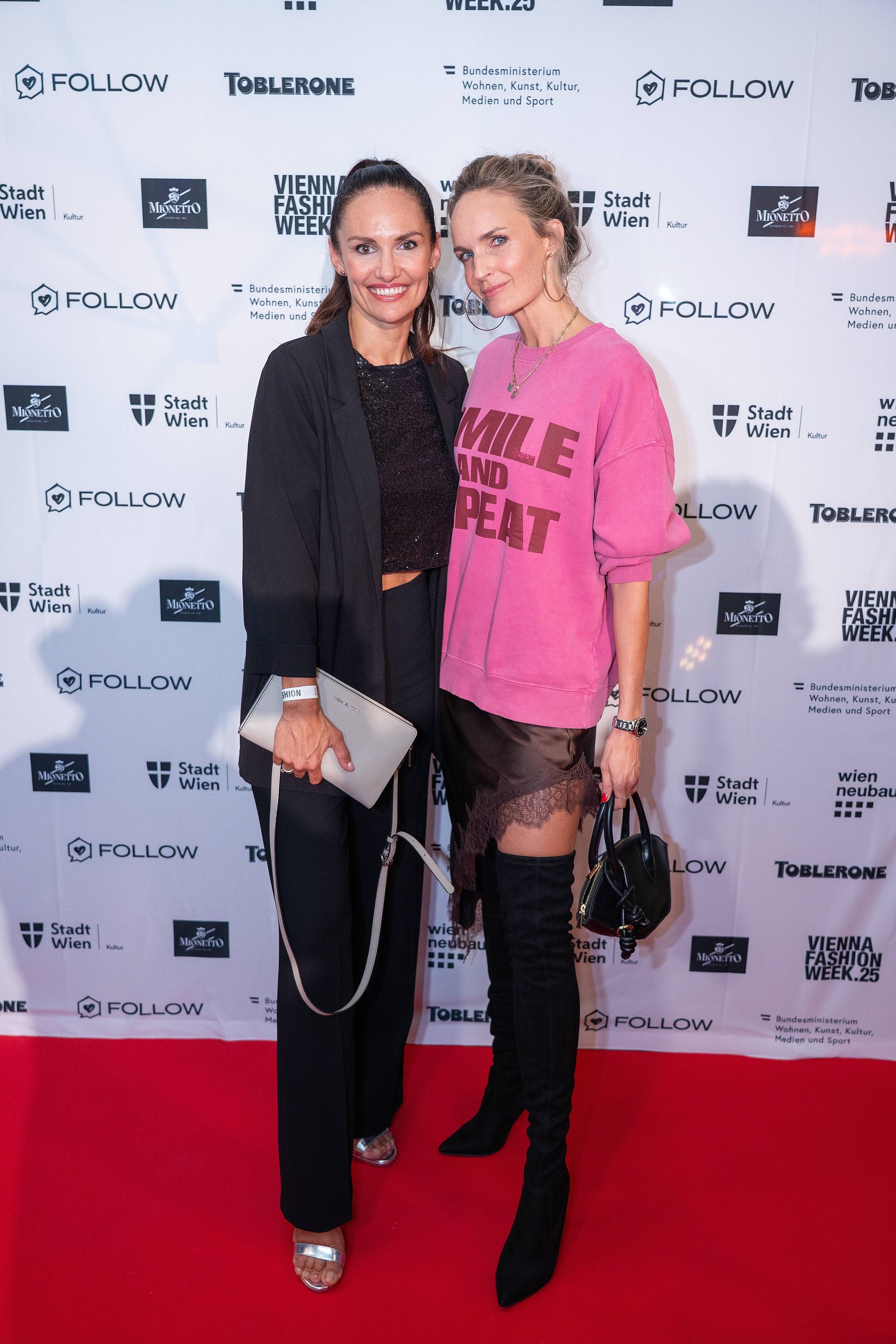 Zwei Frauen posieren lächelnd auf dem roten Teppich bei der Vienna Fashion Week.