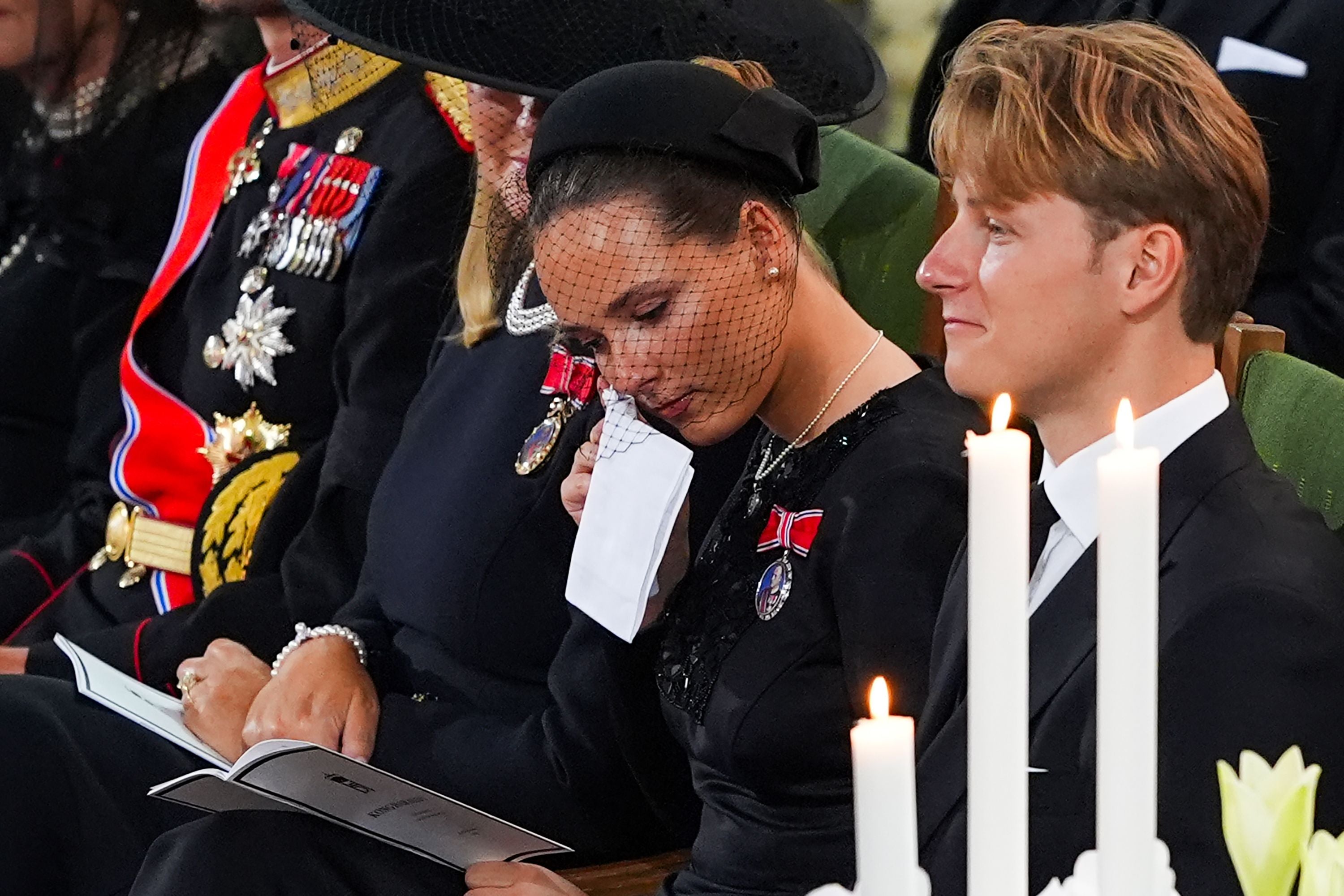 Trauernde Personen in schwarzer Kleidung sitzen in einer Kirche während eines Begräbnisses.