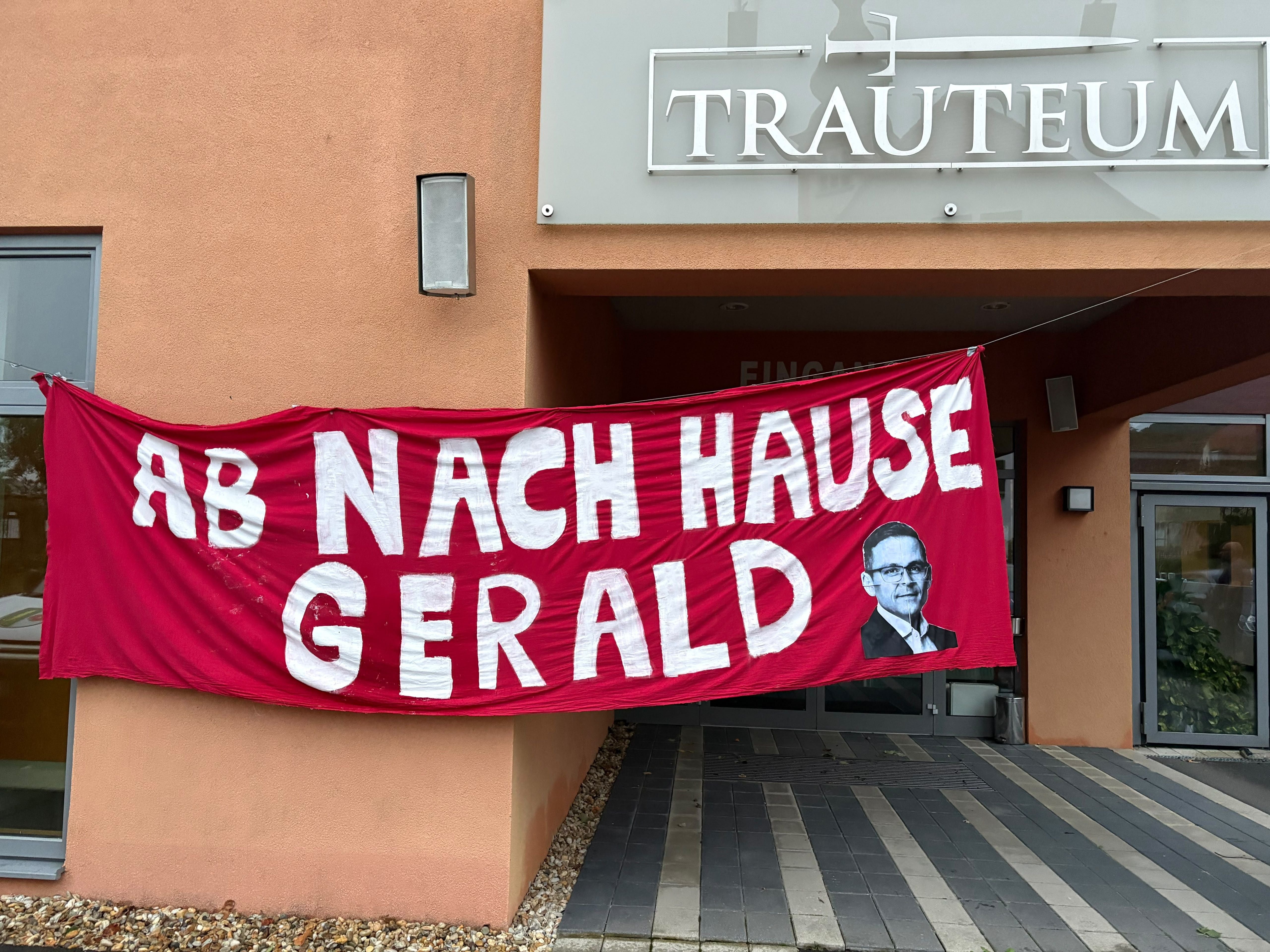 Rotes Banner mit der Aufschrift "Ab nach Hause Gerald" und einem Porträt von Gerald Grosz.