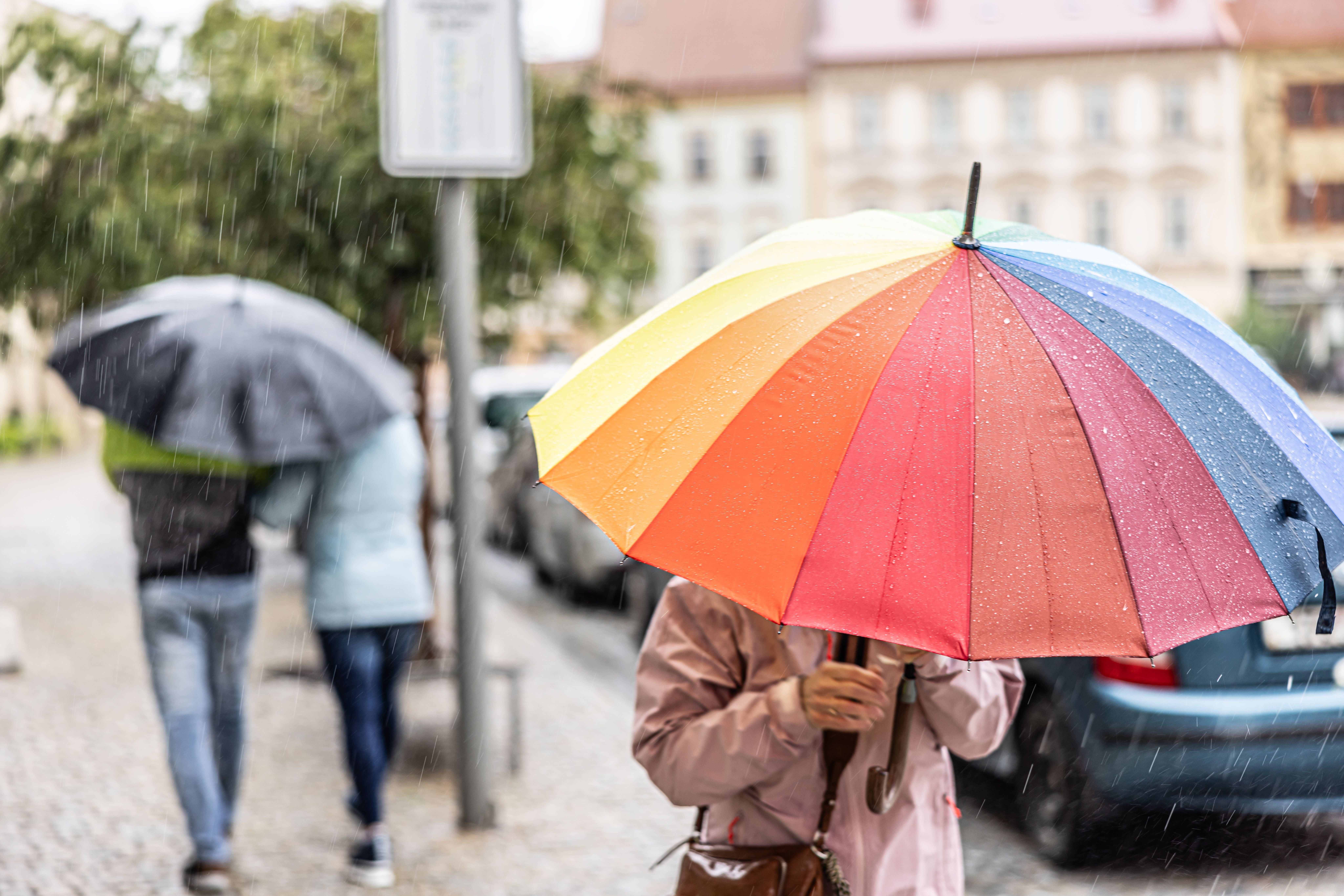 Person mit buntem Regenschirm im Vordergrund, weitere Personen mit Schirmen im Regen im Hintergrund.
