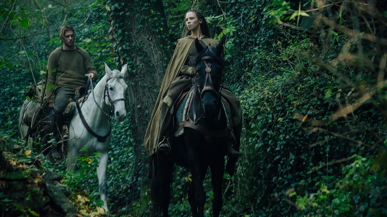 Zwei Personen reiten auf Pferden durch einen dichten, grünen Wald.