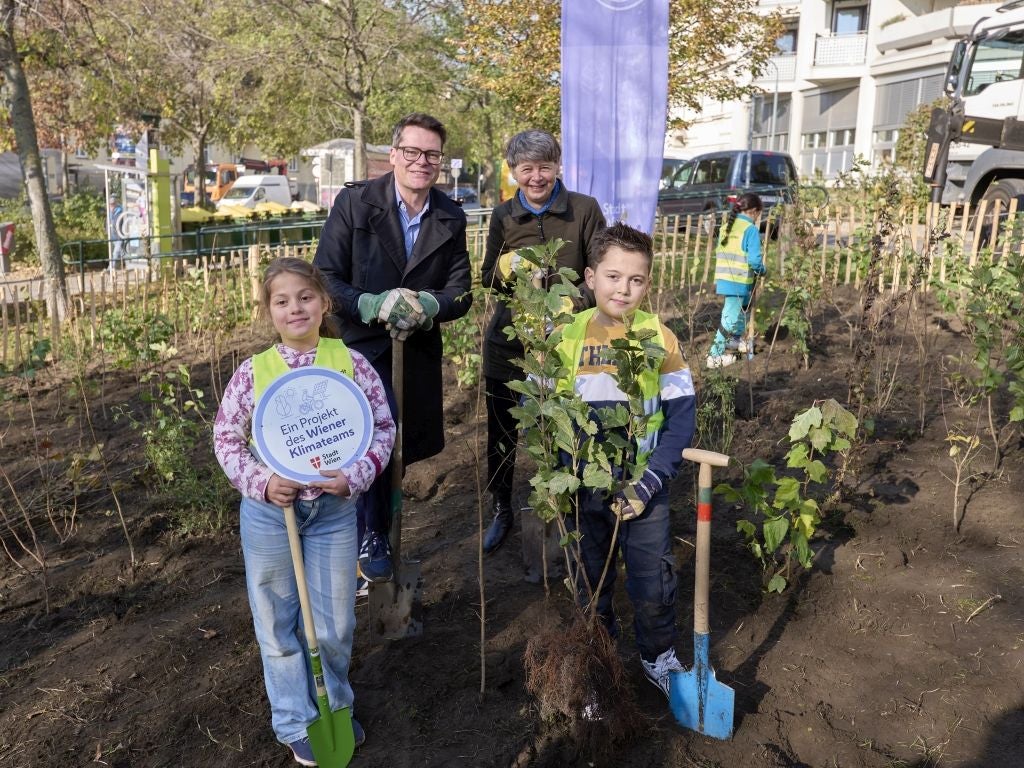 Zwei Kinder und zwei Erwachsene pflanzen Setzlinge in einem Gartenprojekt in Wien.