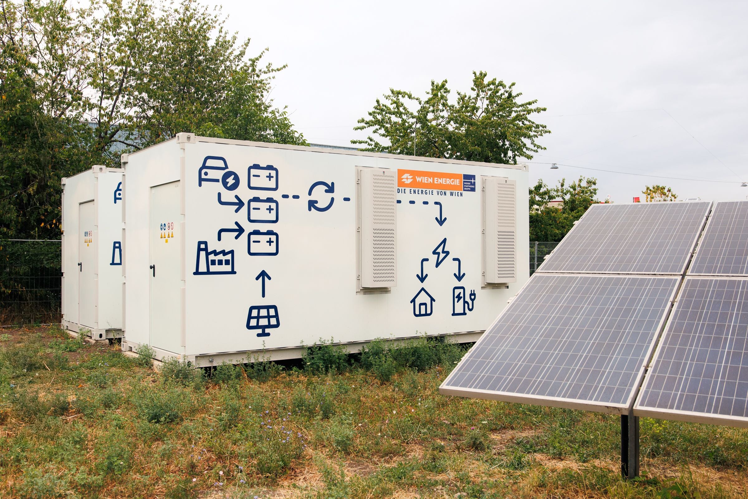 Solarmodule vor einem weißen Container mit Energiespeicher-Symbolen und Wien Energie-Logo.