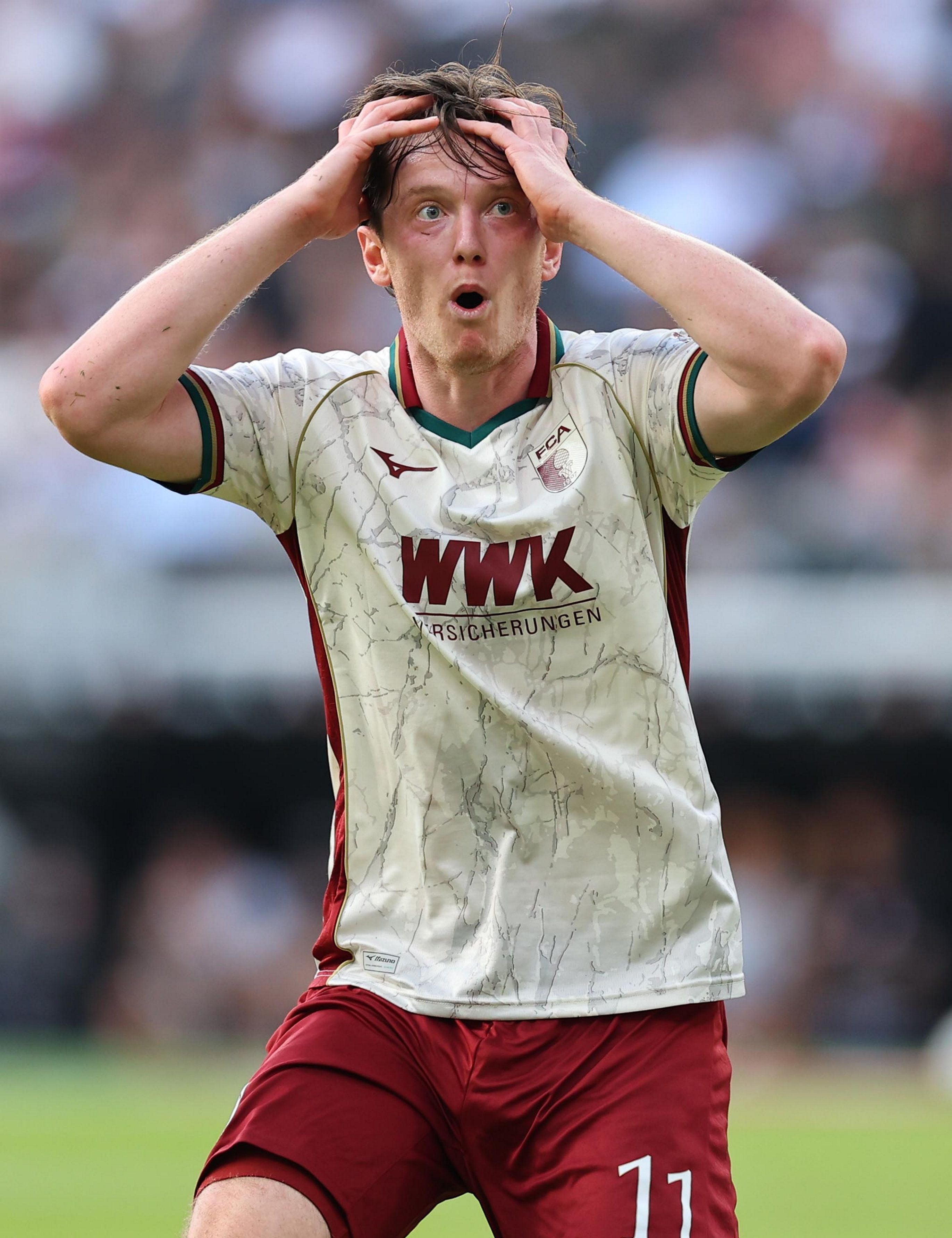 Ein Fußballspieler von Augsburg hält sich überrascht den Kopf und schaut nach vorne.