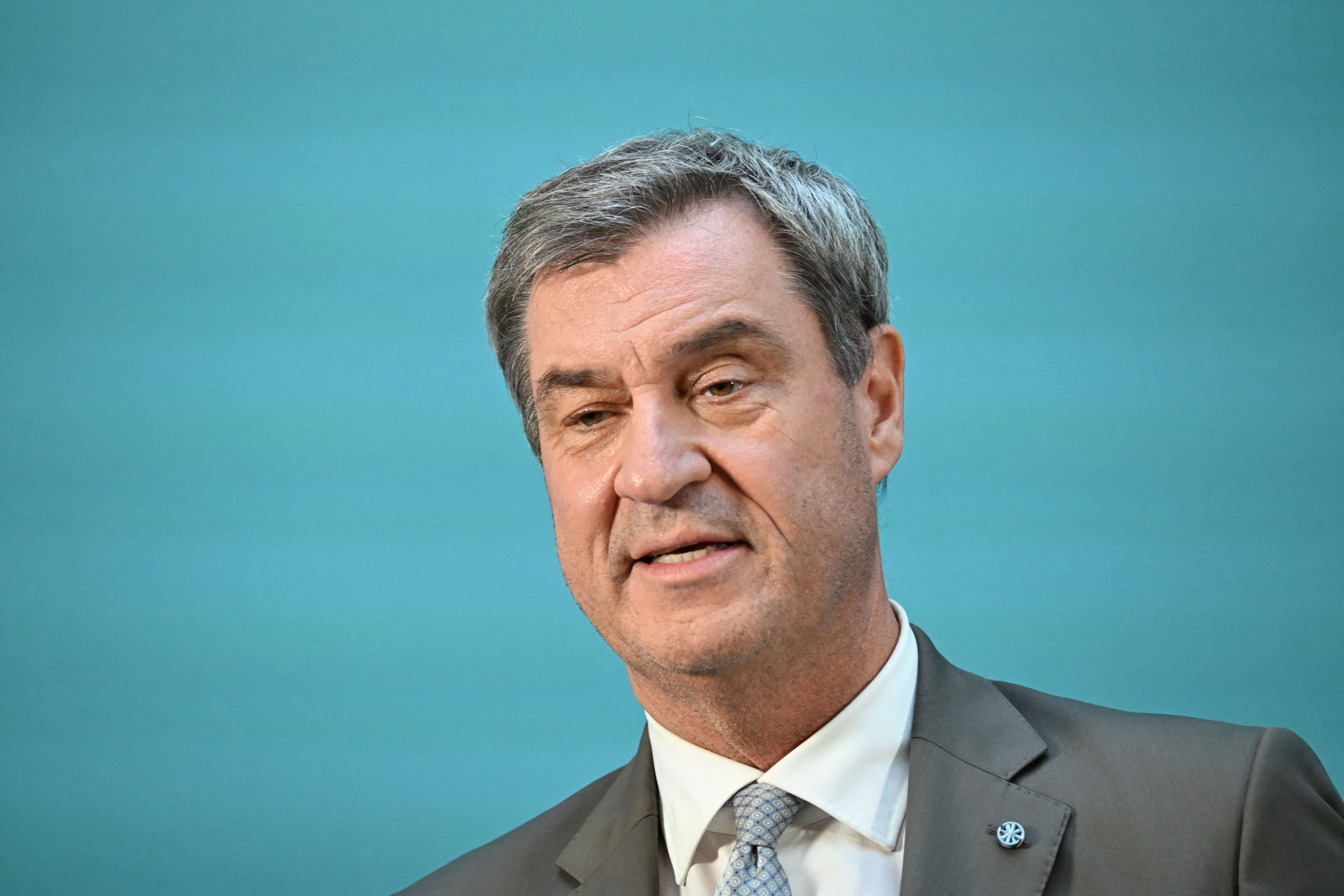 Ein Mann im Anzug spricht vor blauem Hintergrund bei einer Pressekonferenz.