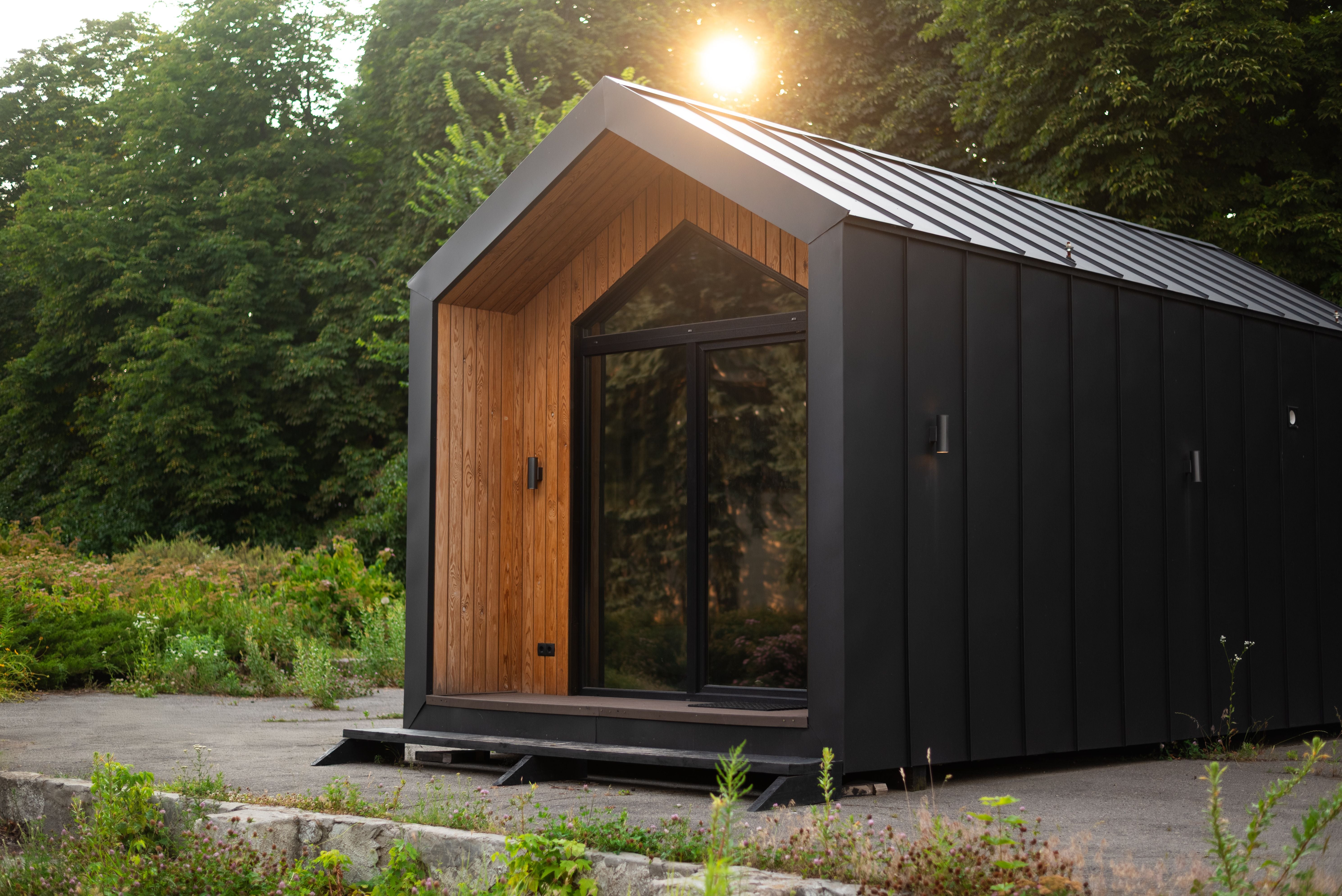 Modernes Tiny House mit Holz- und schwarzer Metallfassade im Grünen bei Abendsonne.