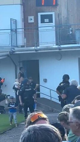 Mehrere Polizisten und Menschen vor einem Gebäude, einige Gesichter sind verpixelt.