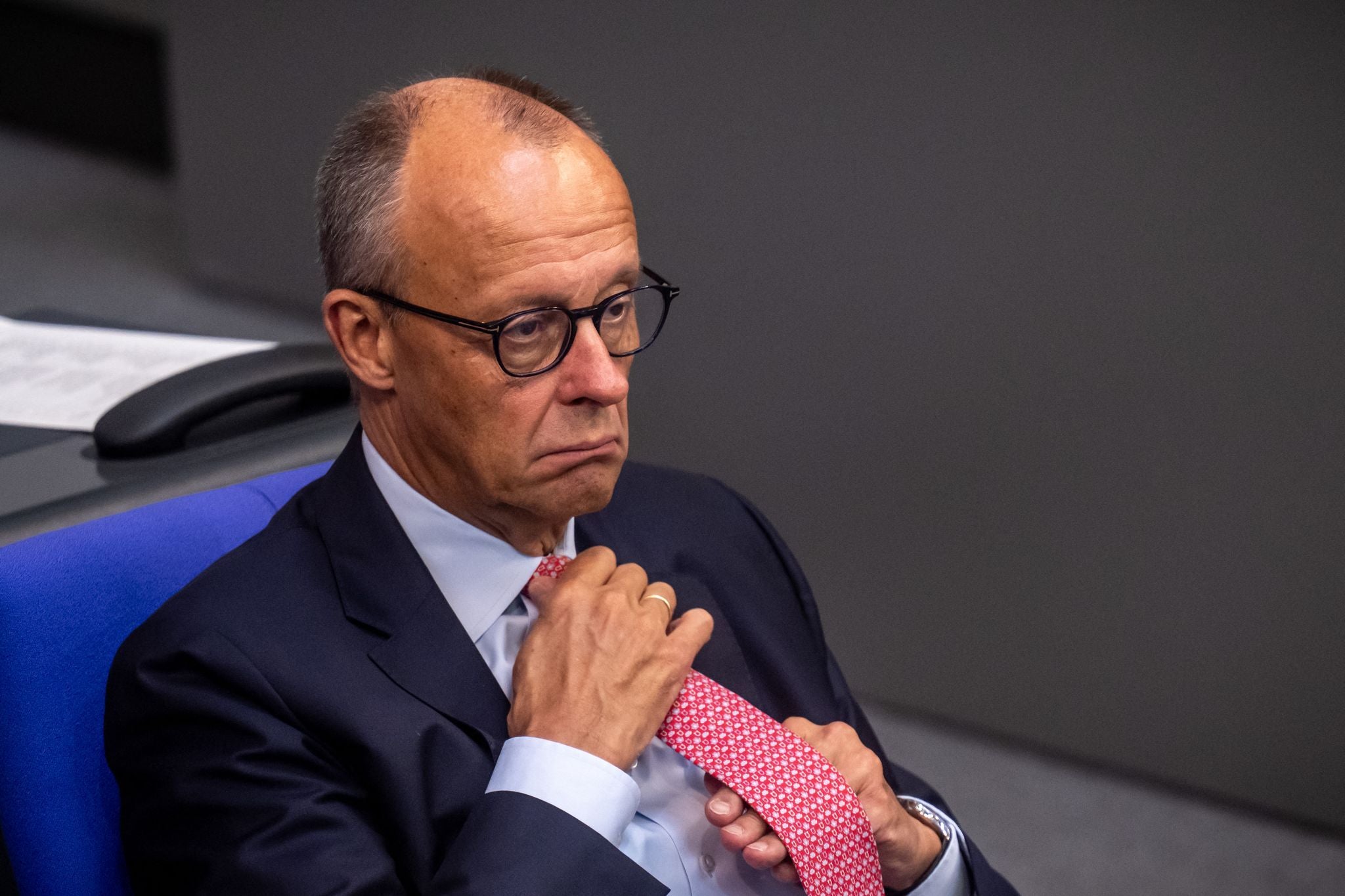 Ein Mann im Anzug sitzt nachdenklich und richtet seine rosafarbene Krawatte.