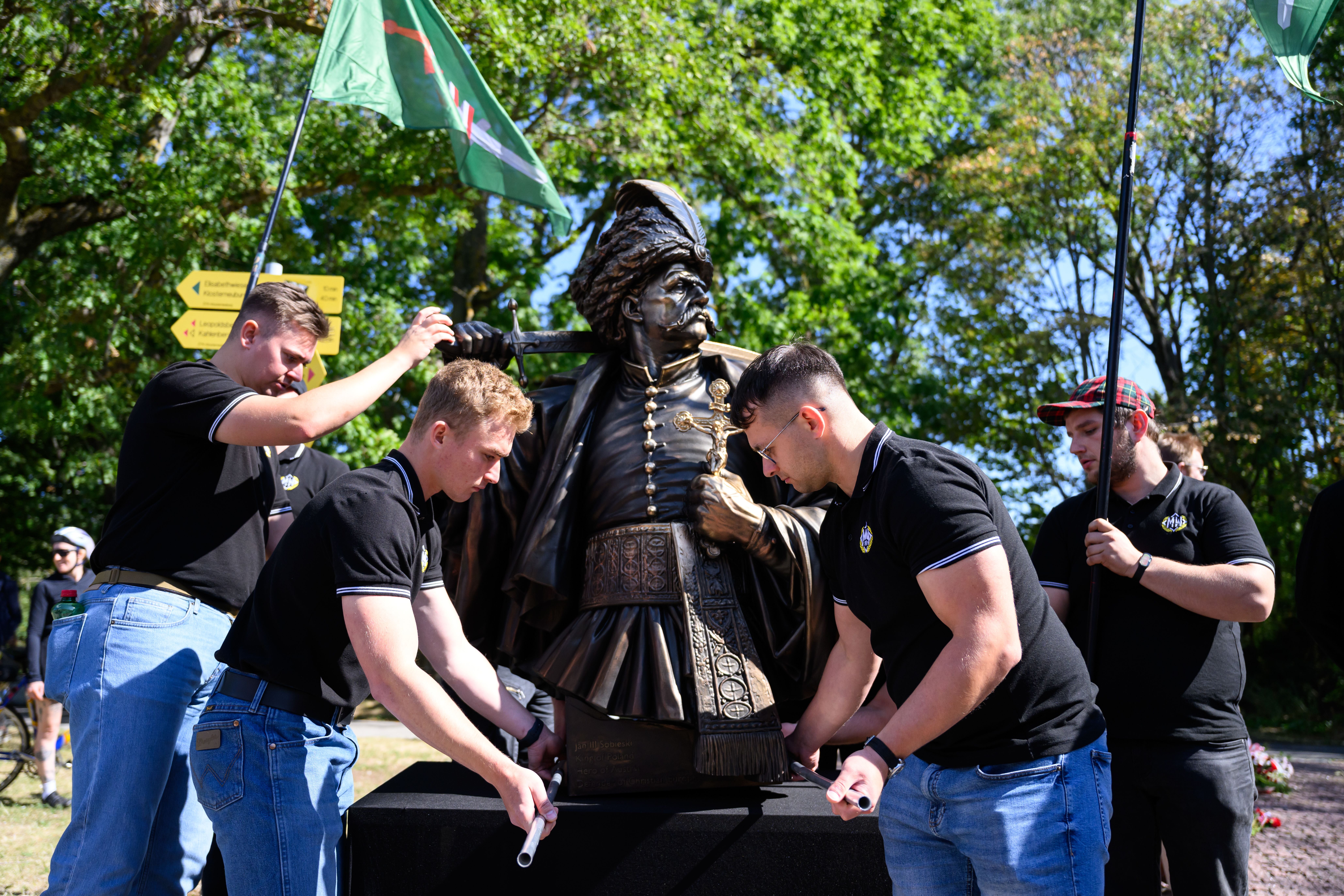 Vier Männer stellen eine Sobieski-Statue bei einer Versammlung im Freien auf.