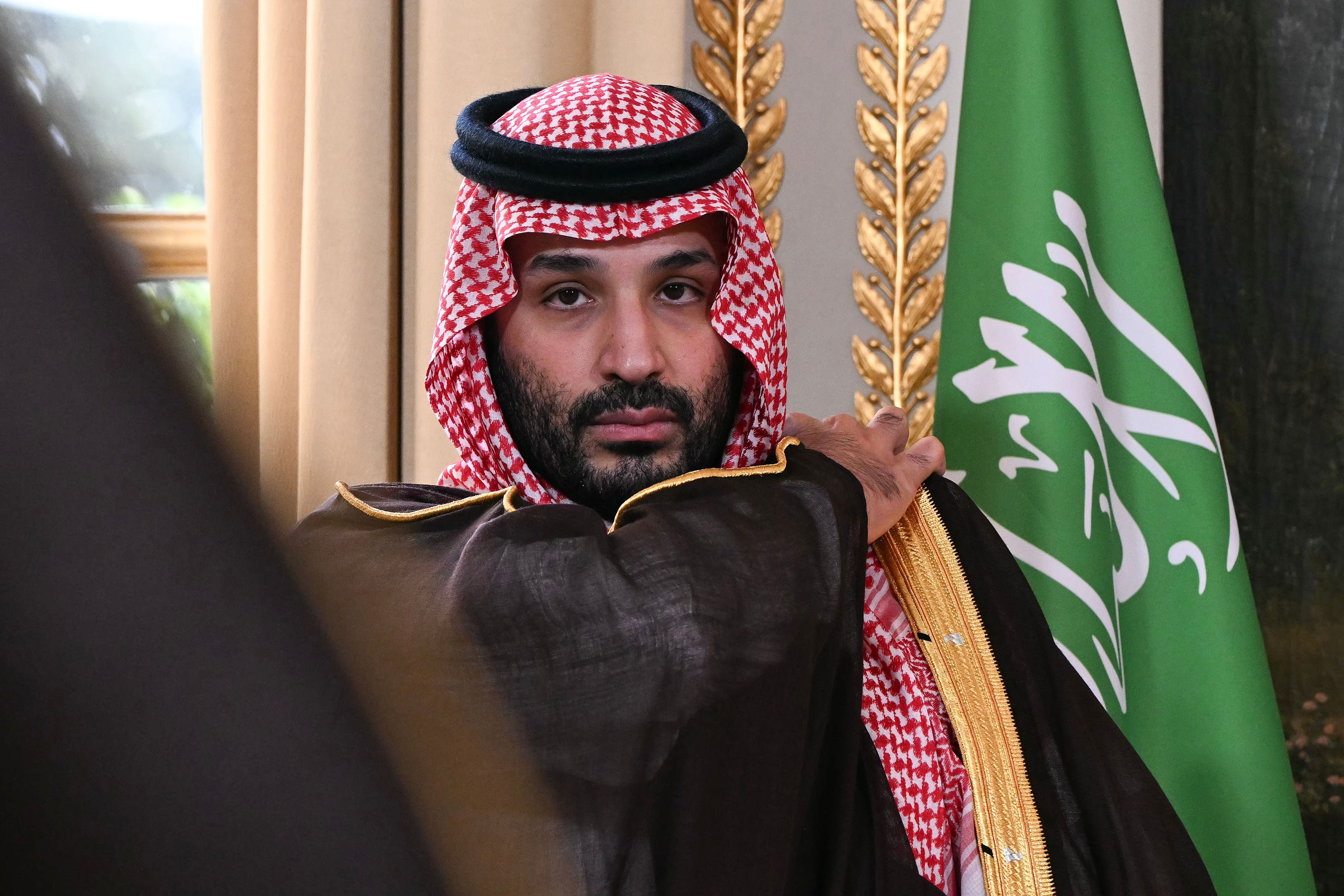 Ein Mann in traditioneller saudi-arabischer Kleidung steht vor einer saudischen Flagge.