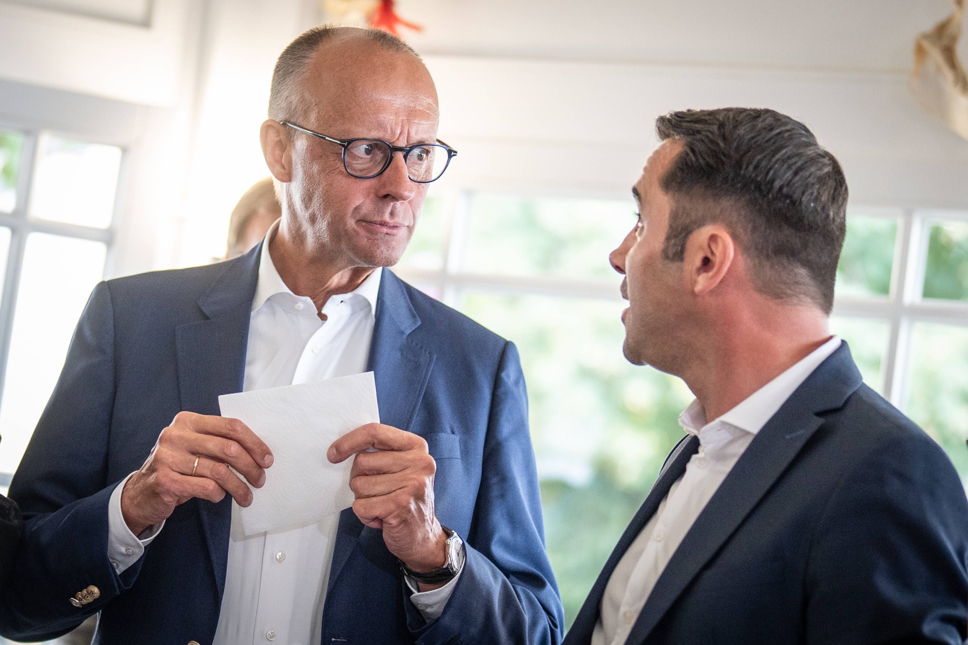 Zwei Männer im Anzug sprechen sich drinnen an, einer hält eine Serviette in der Hand.