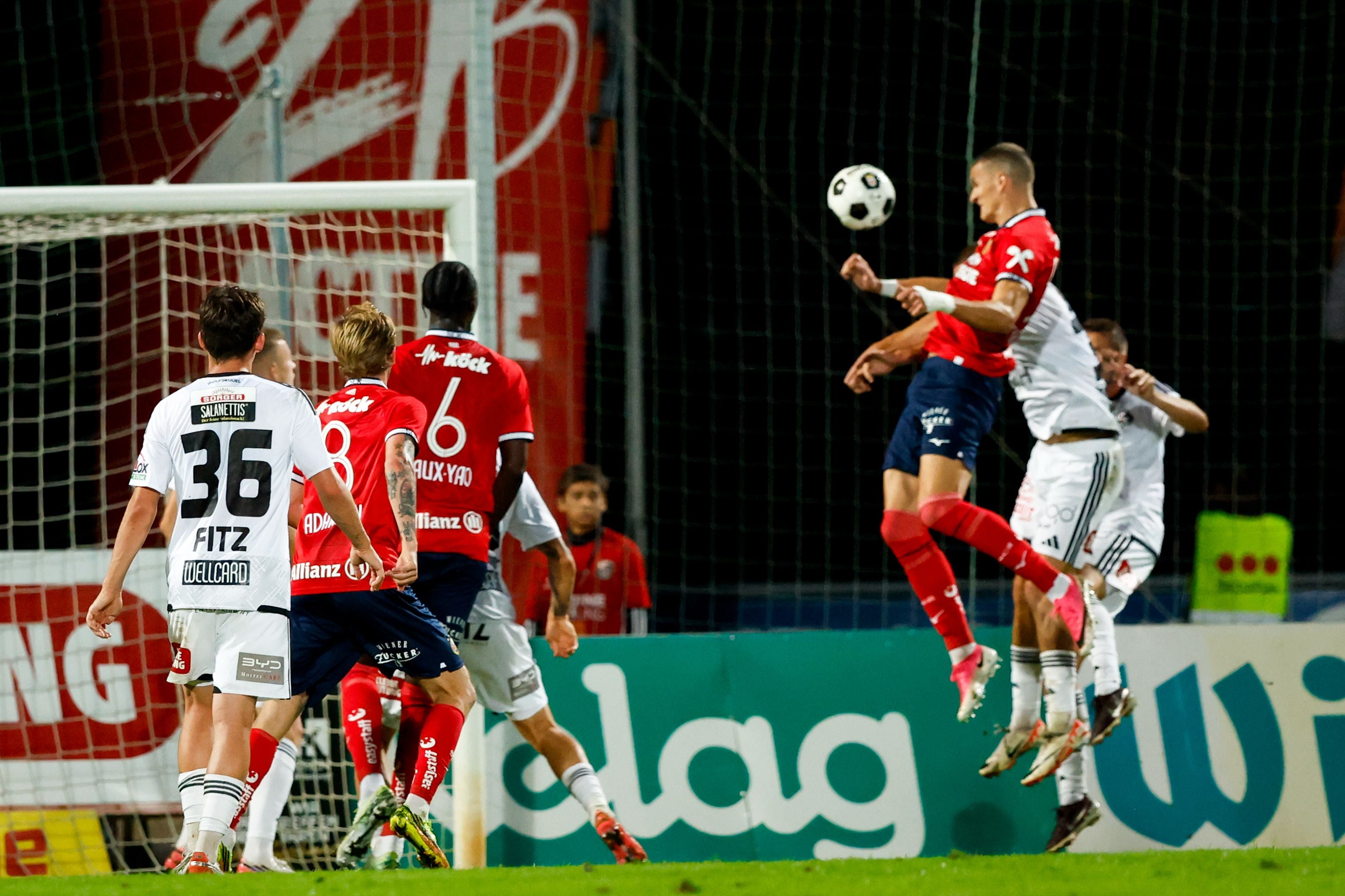 Mehrere Fußballspieler kämpfen vor dem Tor um den Ball, einer springt zum Kopfball.